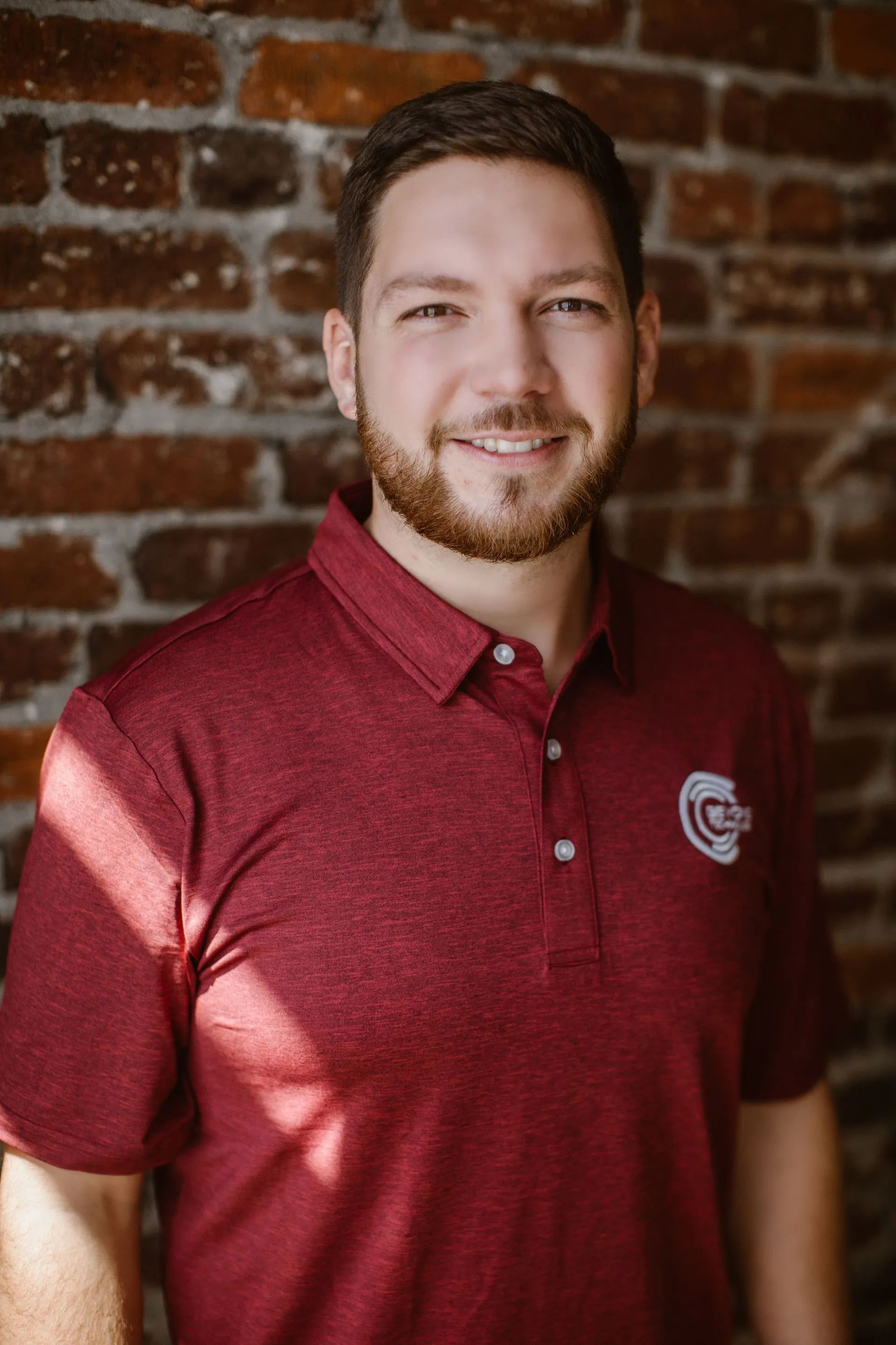 Matt Edmonds, CEO of Beyond Technology, smiling while wearing a maroon polo shirt with a Beyond Technology logo, standing in front of a rustic brick wall.