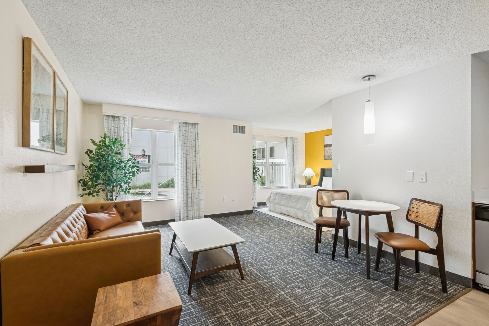 Hotel suite interior with sofa, coffee table, dining set, bed, and window.