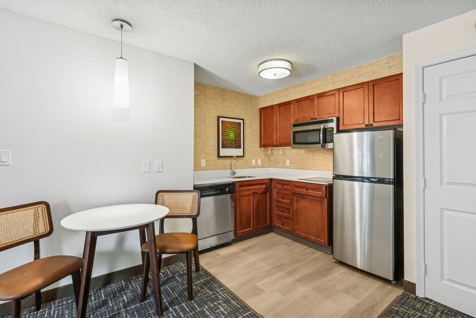 Kitchen with wood cabinets, stainless steel appliances, small table and chairs, and a pendant light.