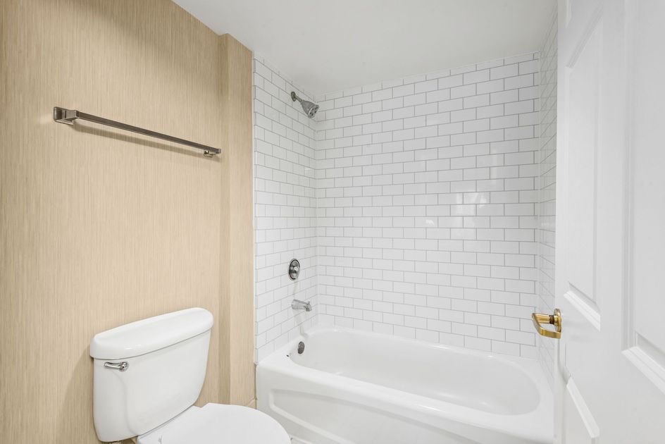 Bathroom interior with a white bathtub, toilet, and white tile shower.