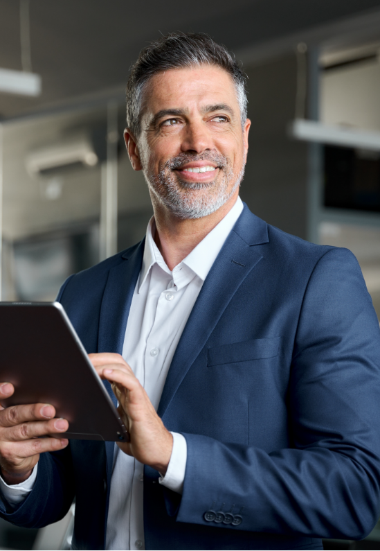 Smiling man in a blue suit holding a tablet, looking upward in an office setting.
