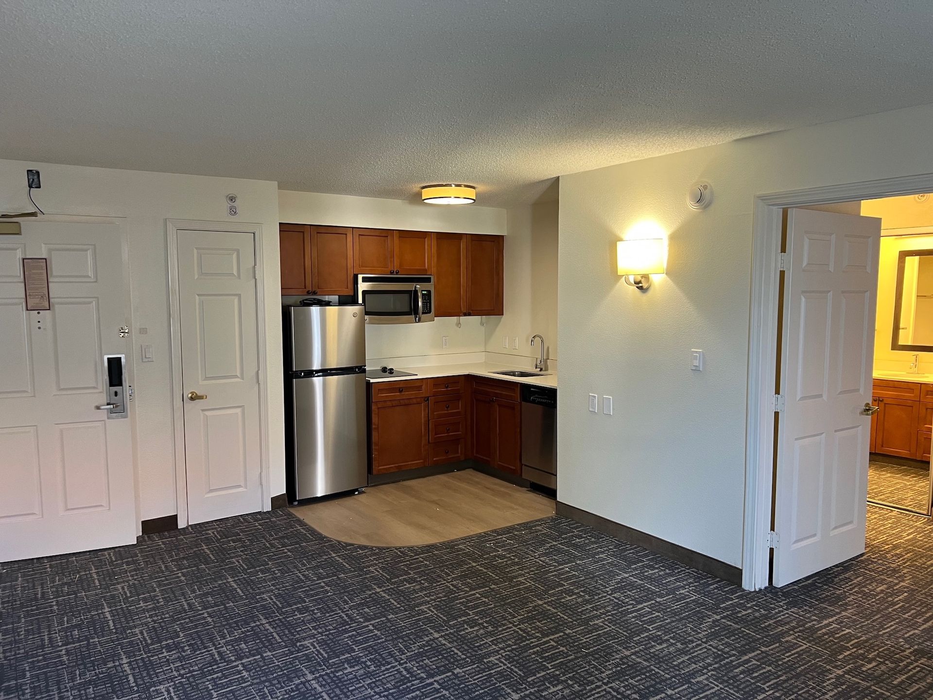 Small kitchen with stainless steel appliances and wooden cabinets, in a hotel room setting.