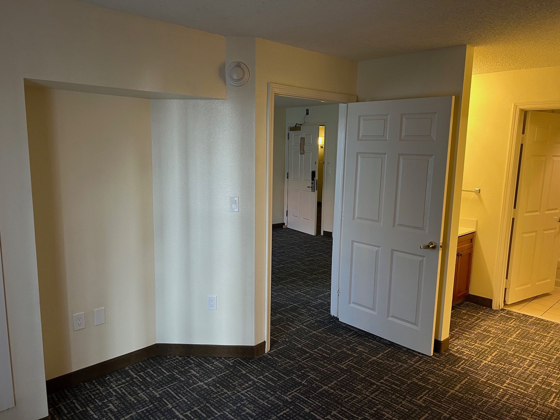 Interior view of a hotel room with doors to hallway and closet. Carpet and neutral wall colors.