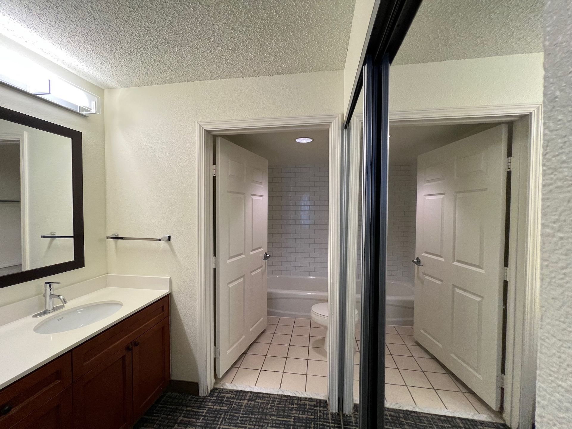 Bathroom with vanity, mirror, and two doors leading to a toilet and tub/shower area.