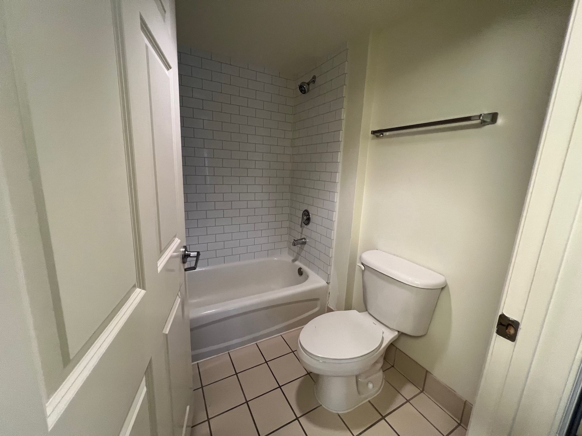 Small bathroom with toilet, bathtub, and tiled walls. White and beige tones.