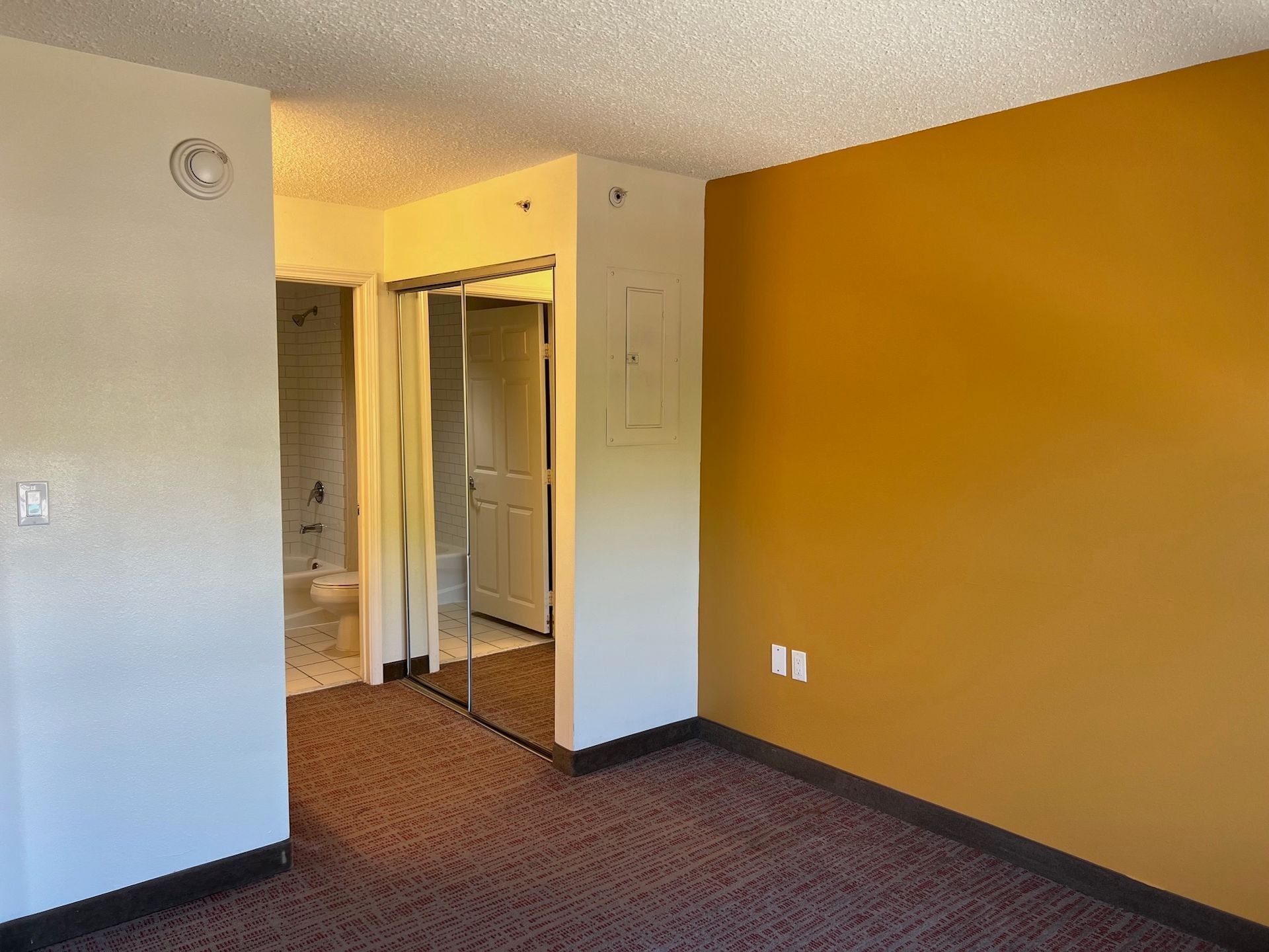 Bedroom interior with brown carpet, mirrored closet, and mustard-colored wall.