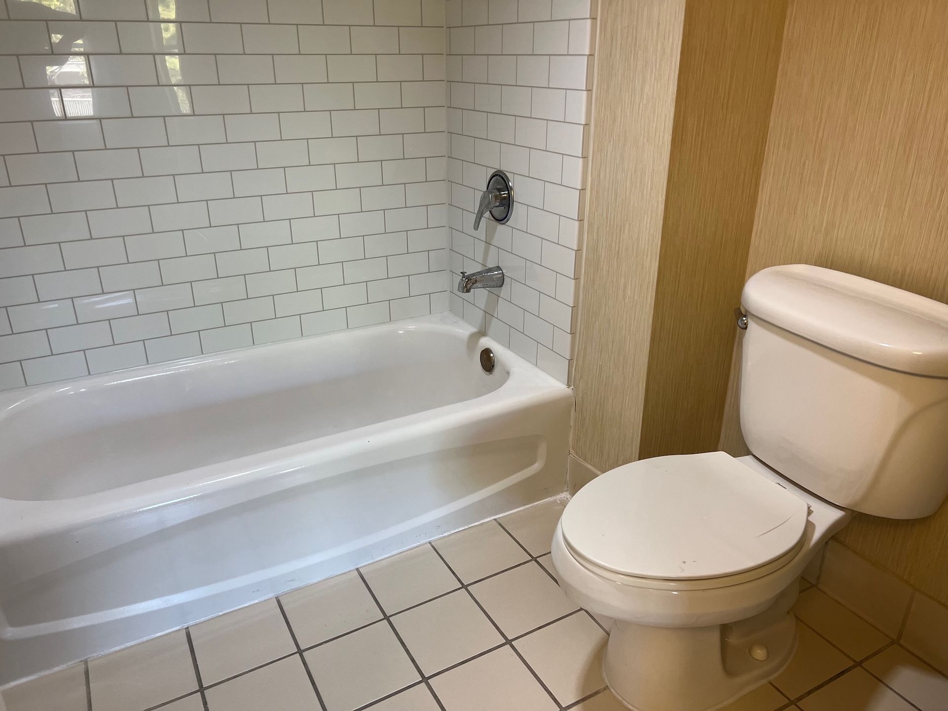 Bathroom with white bathtub, toilet, and subway tile walls. Light-colored tile floor.