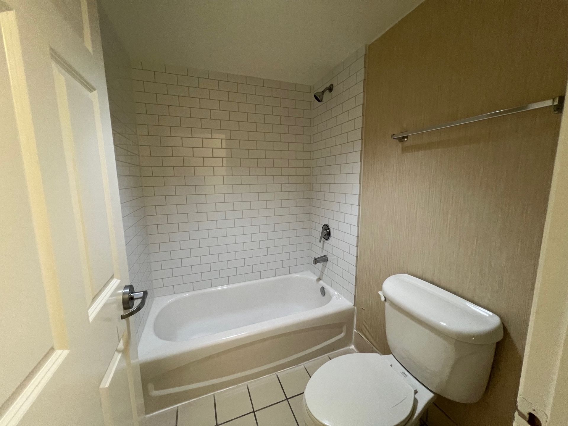 Bathroom with tub, toilet, and white tile shower surround.