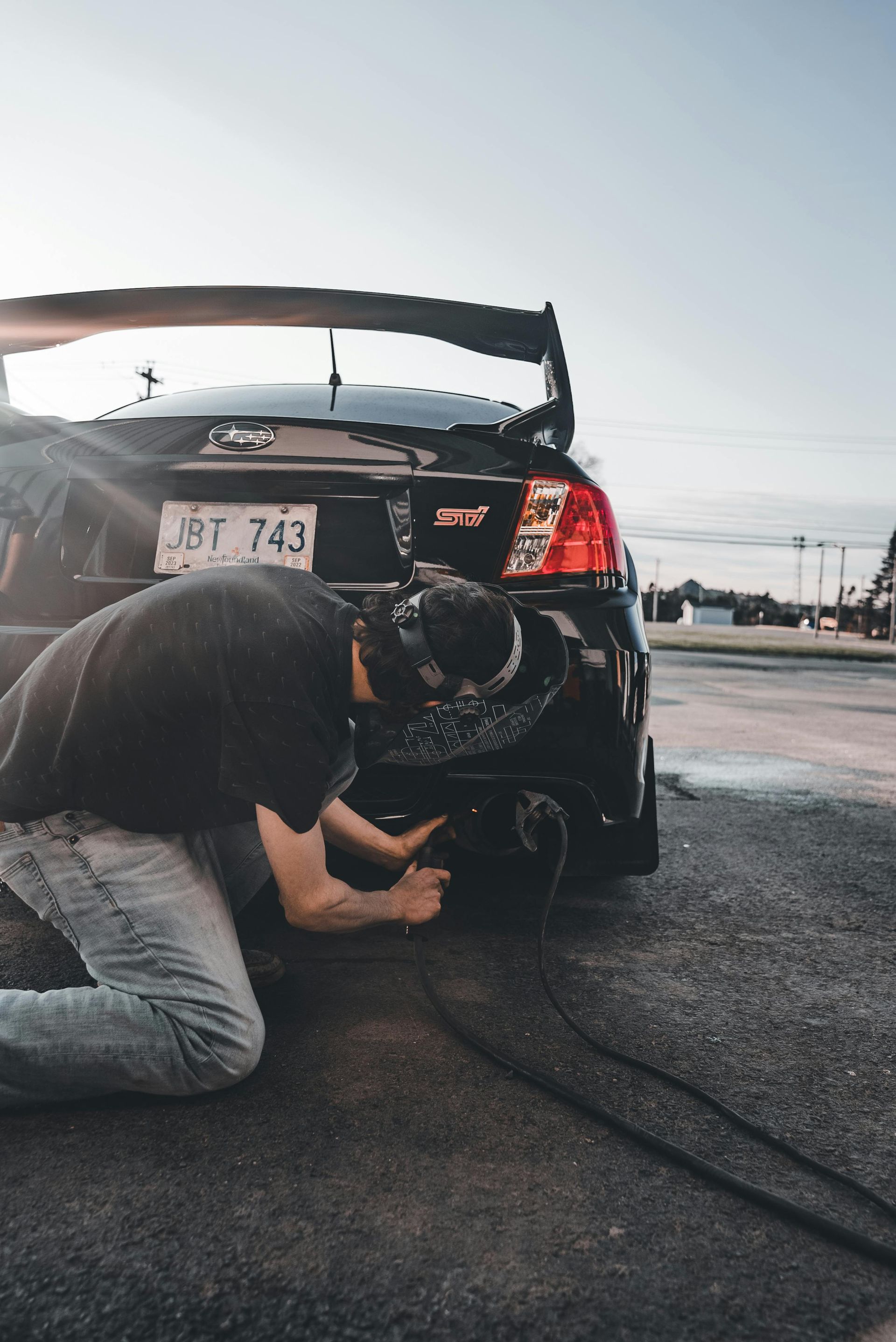 A man is kneeling down in front of a black car.