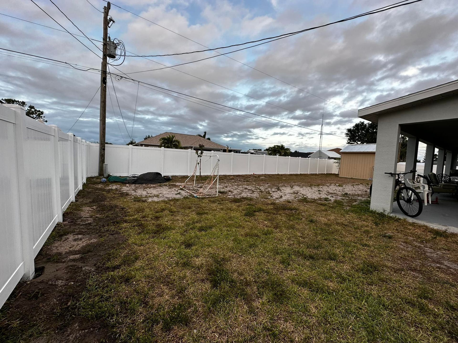 Backyard with white fence, brown grass, power lines, and a covered patio.