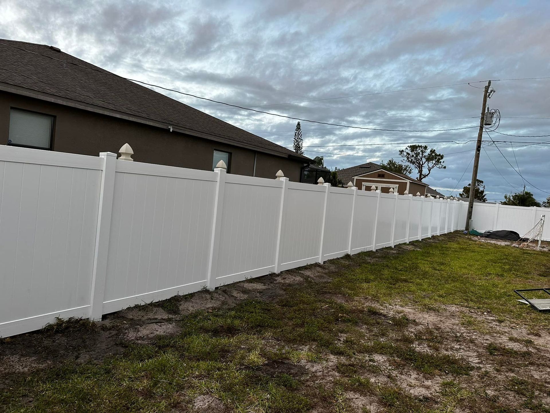 White vinyl fence along a backyard, with a house and cloudy sky in the background.