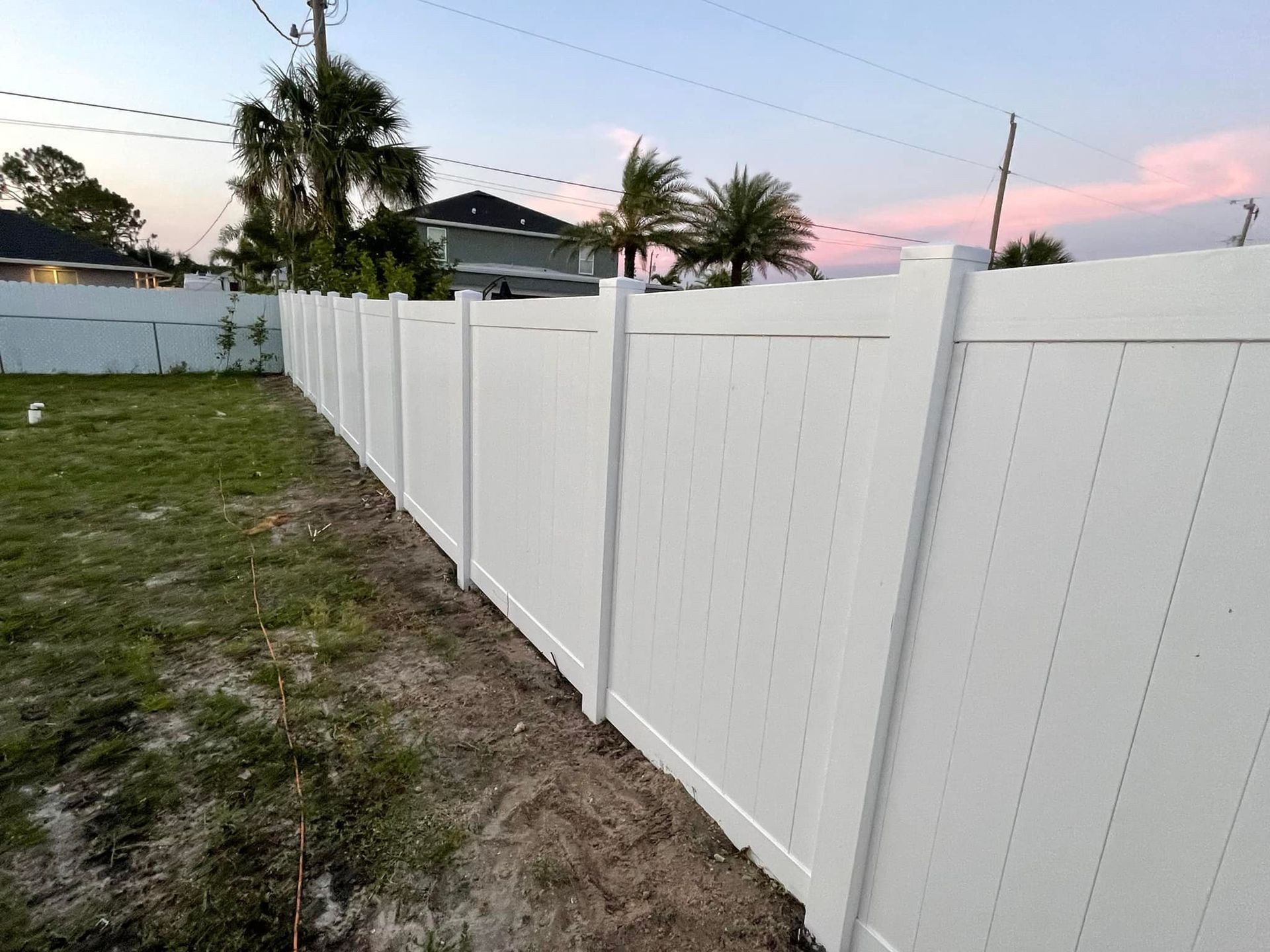 White vinyl fence in backyard under a dusky sky.