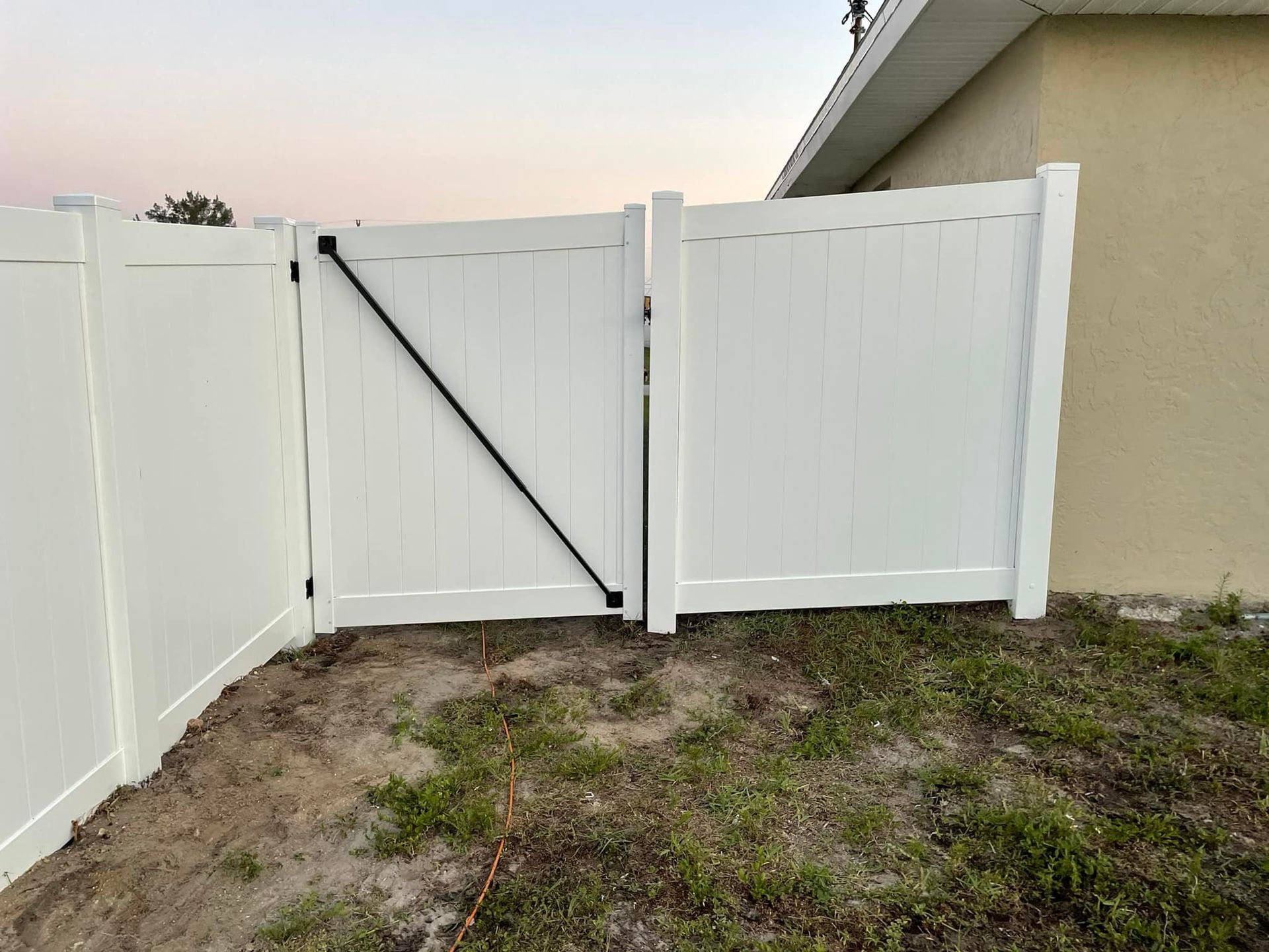 White vinyl fence with a gate, angled black brace. Outdoors, next to building.
