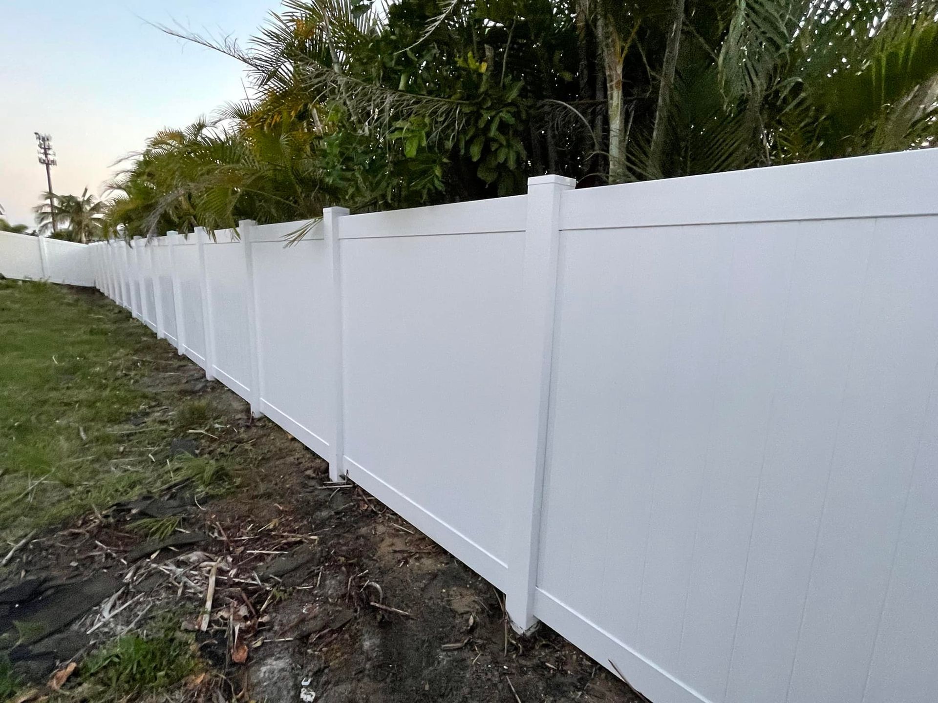 White vinyl privacy fence in front of green grass and foliage.