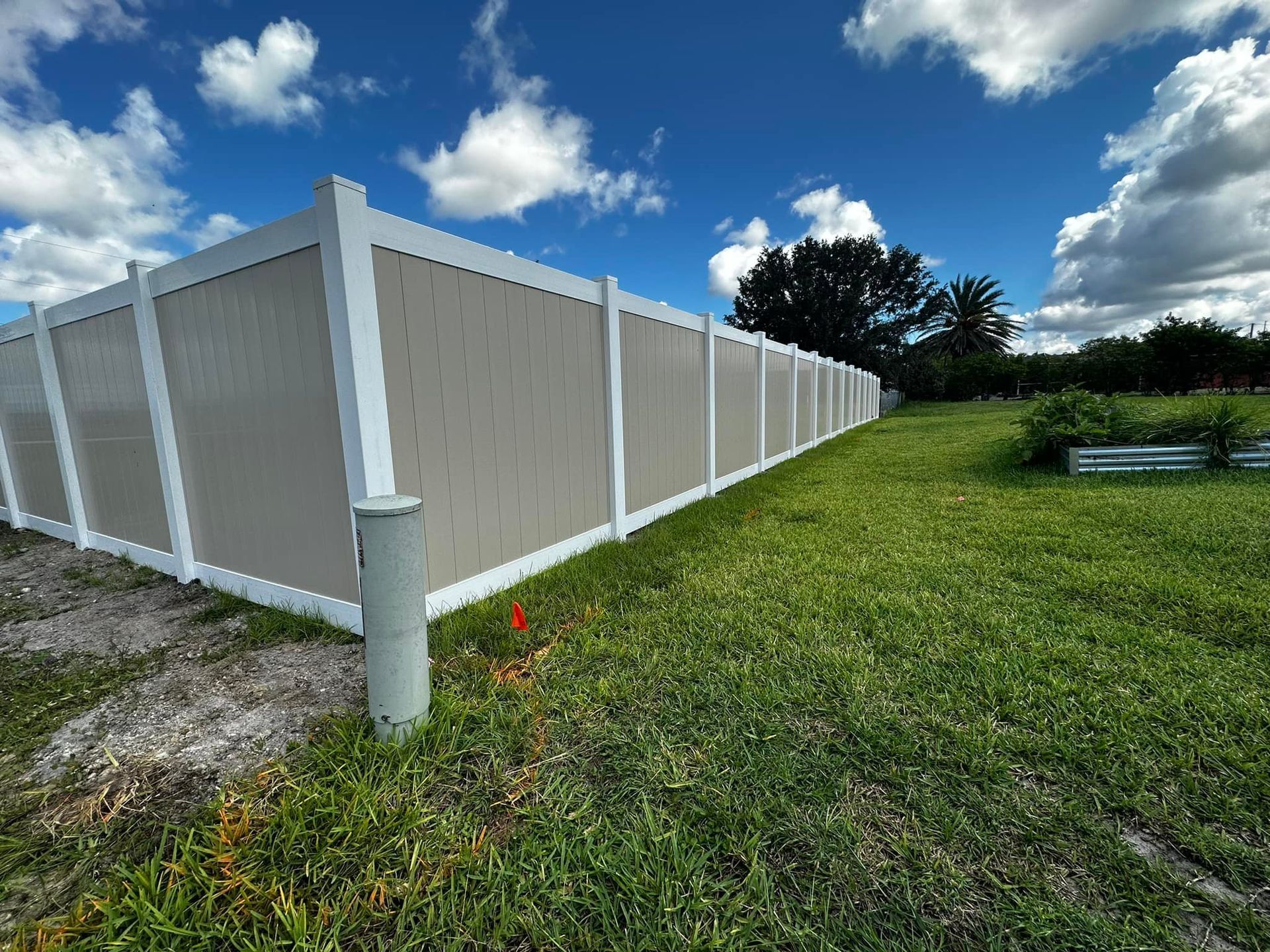 Tan and white vinyl fence around grassy yard under blue sky with clouds.