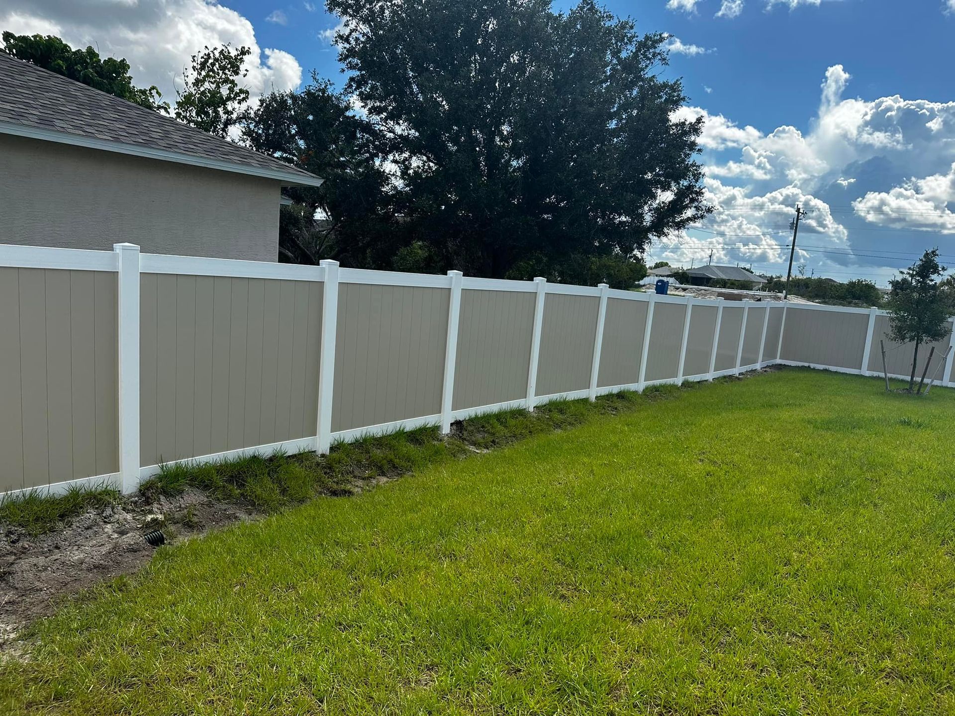 Tan and white vinyl privacy fence in backyard with green grass.