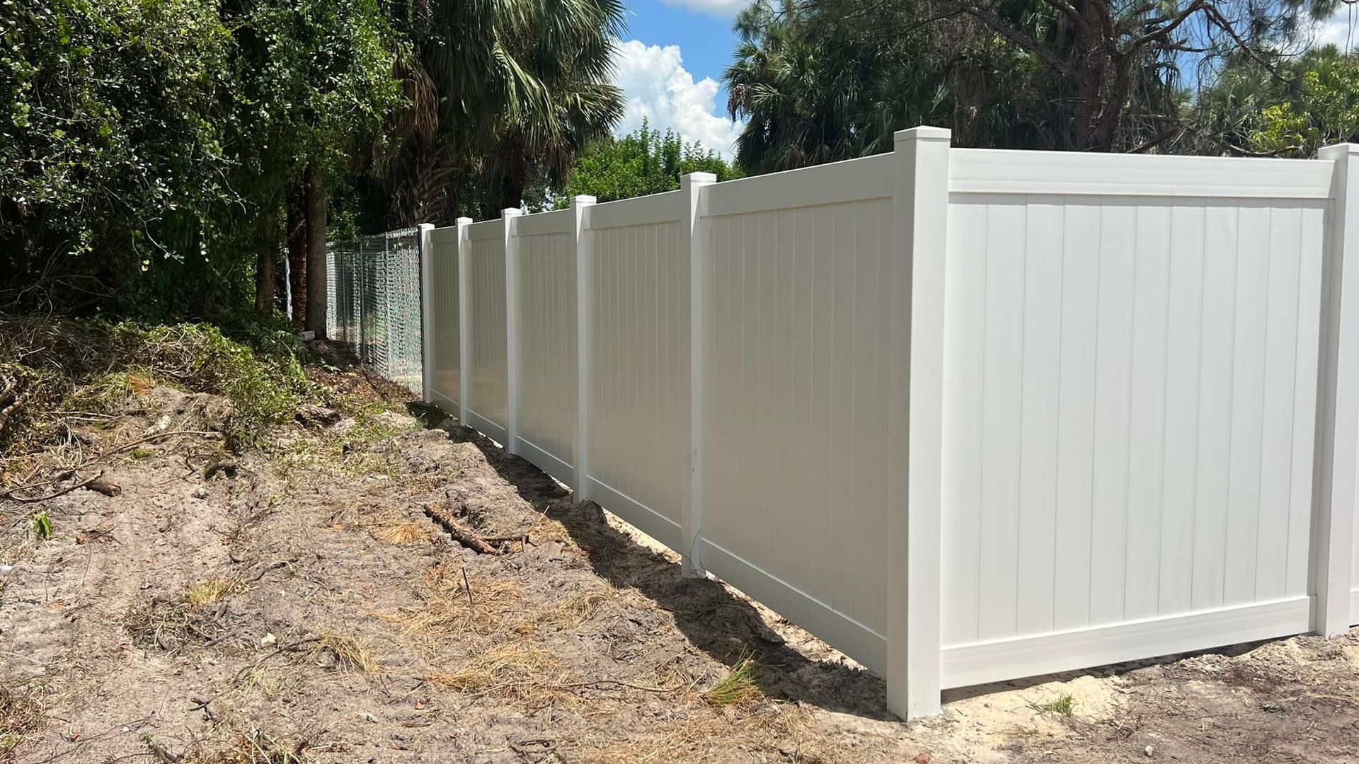 White vinyl privacy fence in a sunny outdoor setting, with trees in the background.