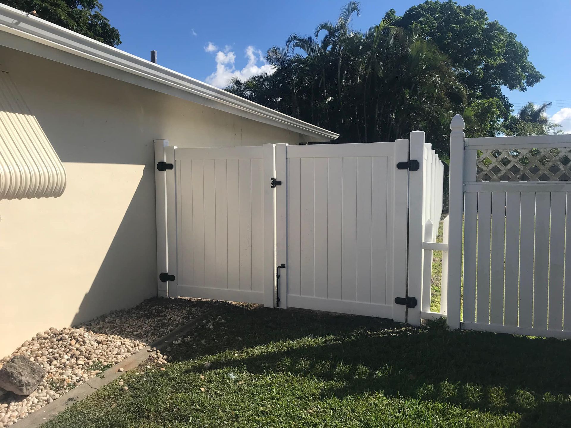 White vinyl gate in a yard, adjacent to a beige house, with a white lattice fence on the right.