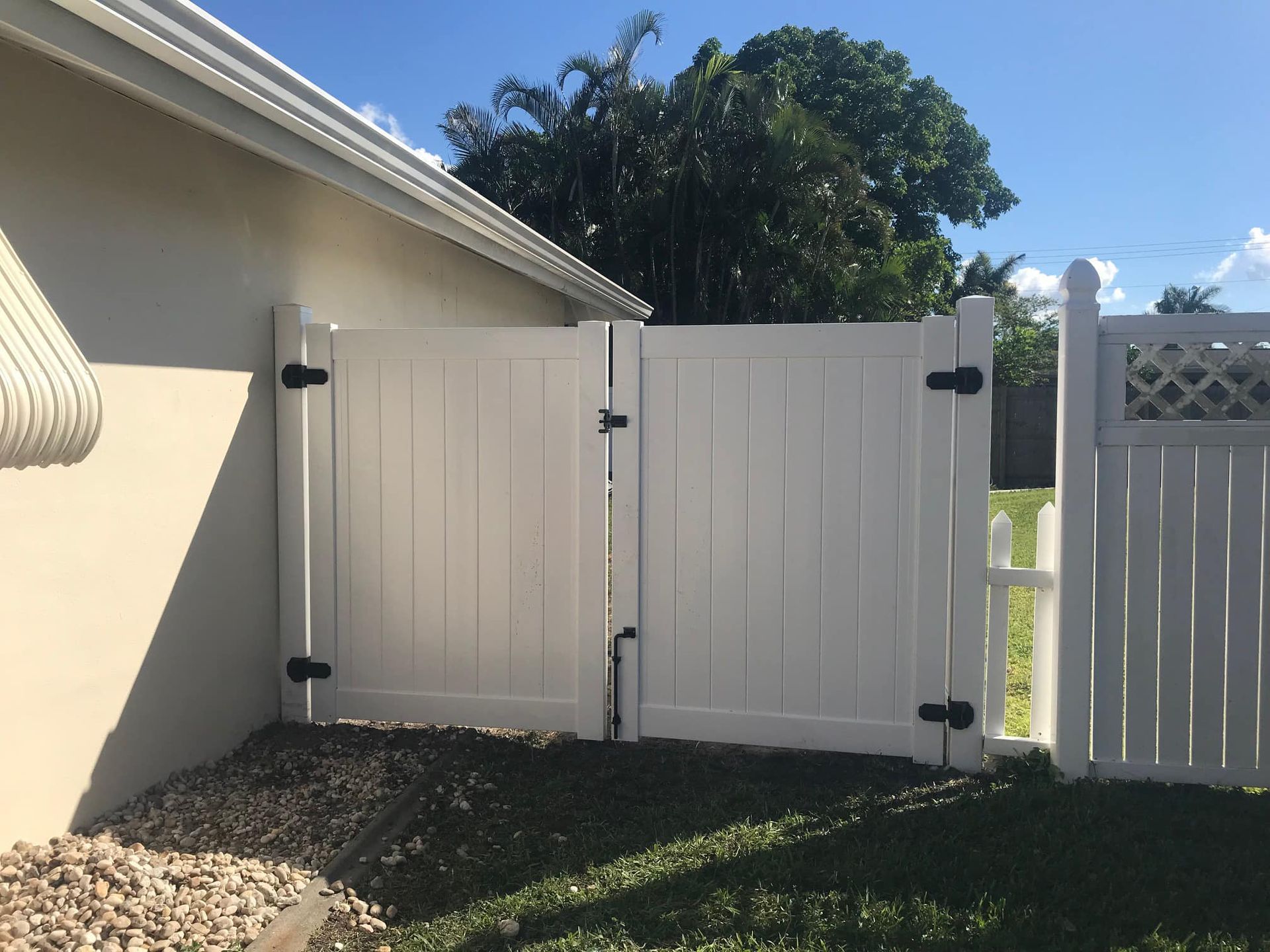 White double gate in a backyard, next to a house and a white fence.
