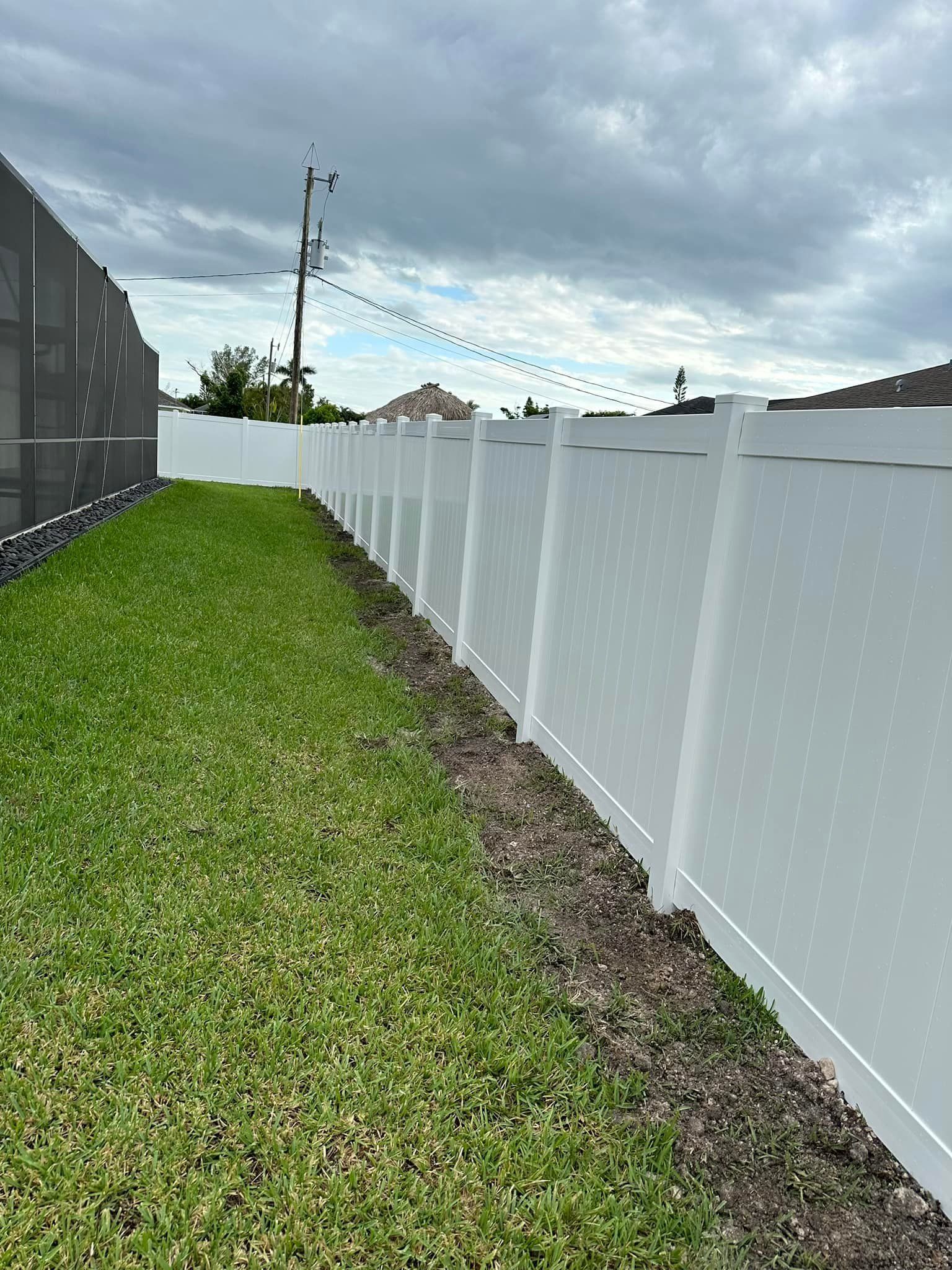 White fence bordering green lawn and gravel path under a cloudy sky.