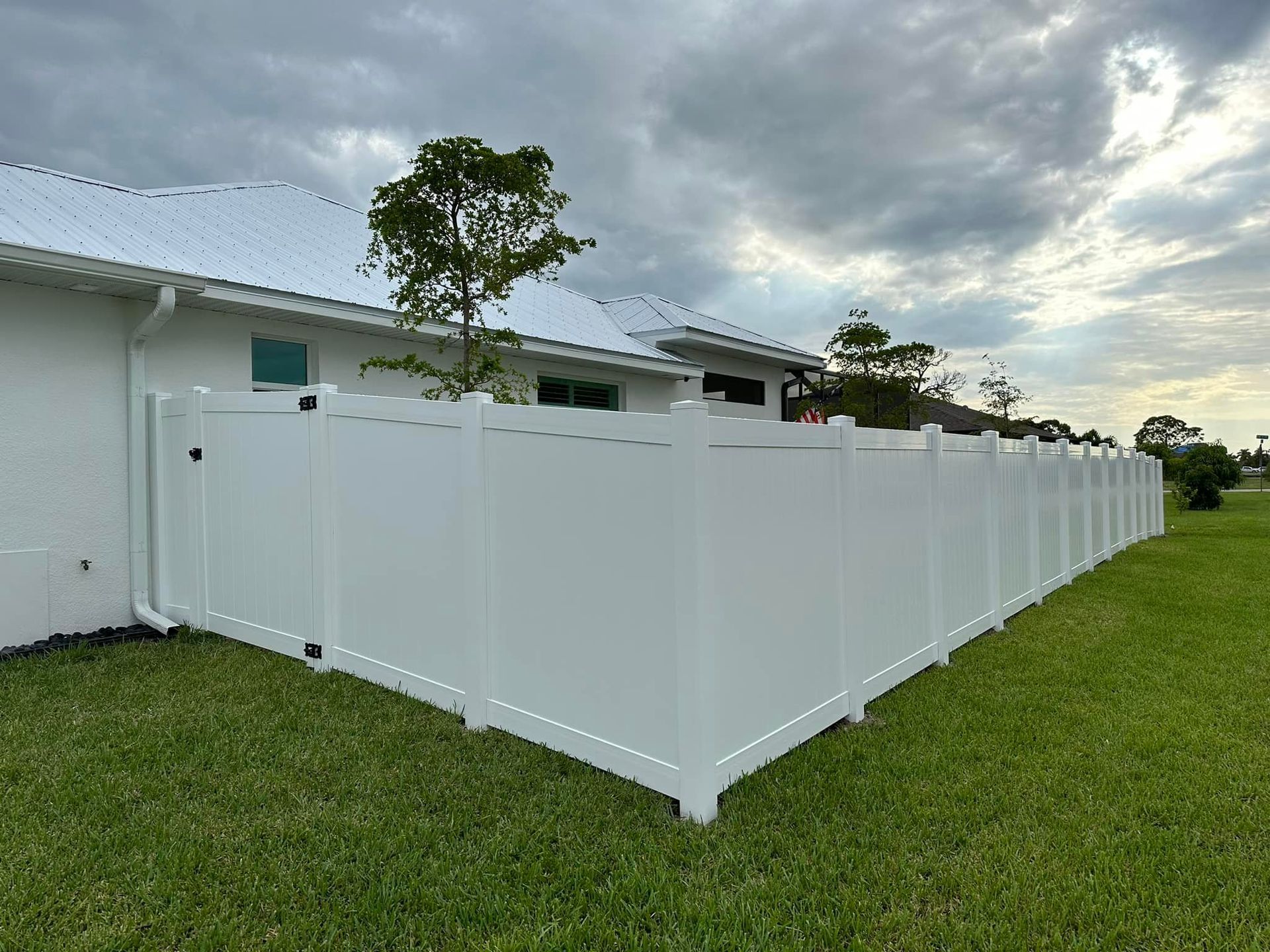 White vinyl privacy fence in a grassy backyard against a house under a cloudy sky.