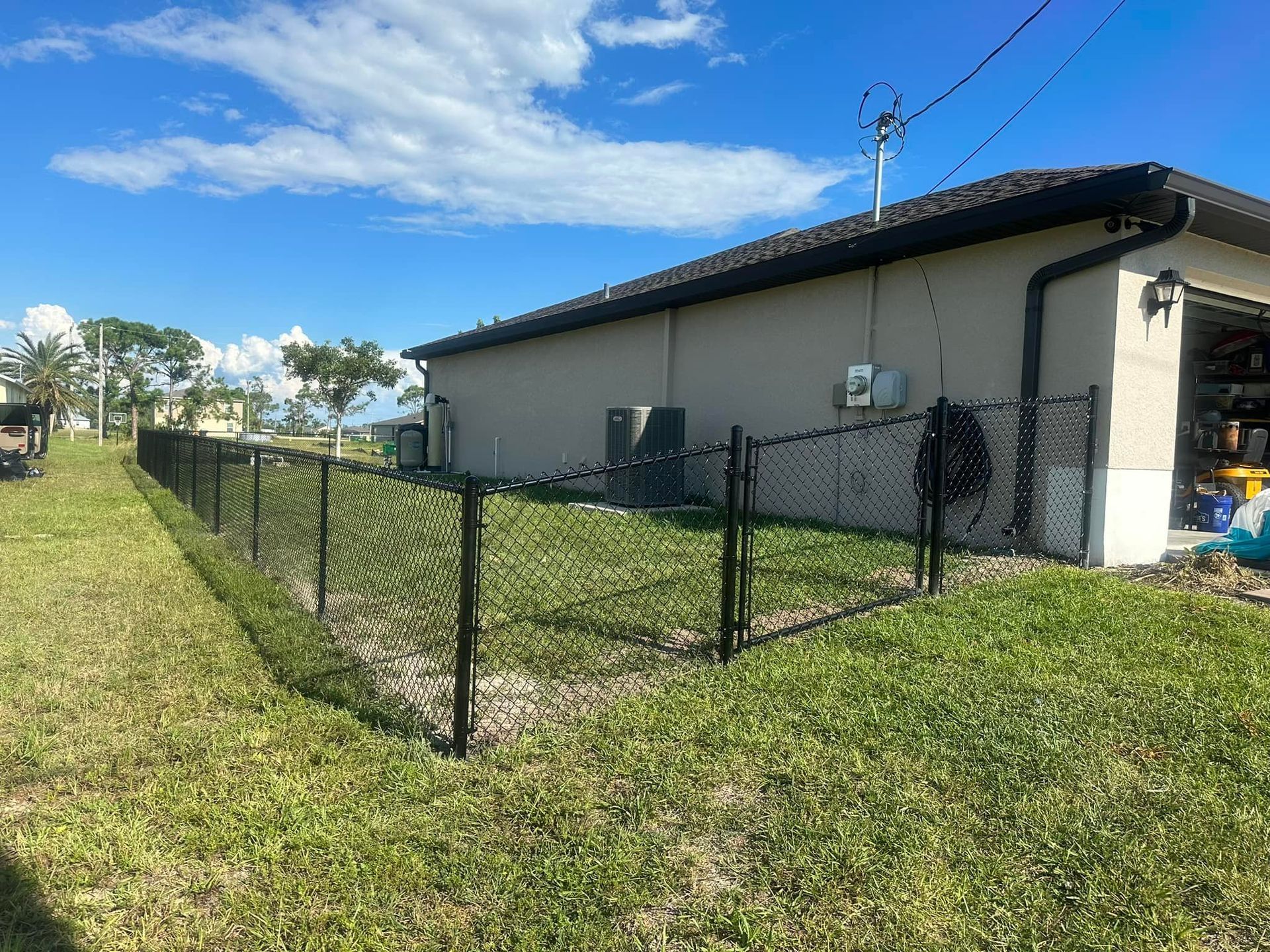 Black chain-link fence around a light-colored building with an AC unit on a sunny day.