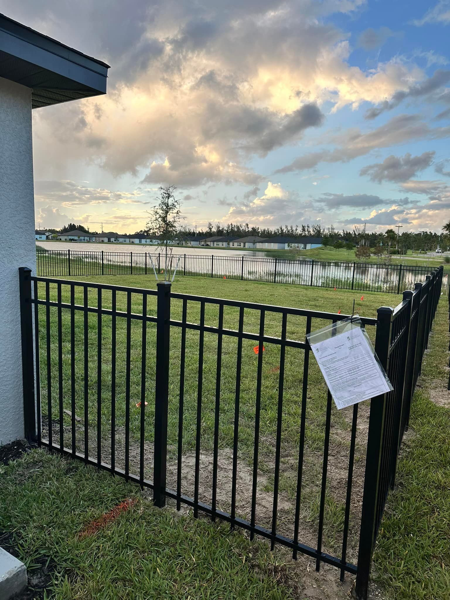 Black metal fence by a house, overlooking a lake under a cloudy sky.