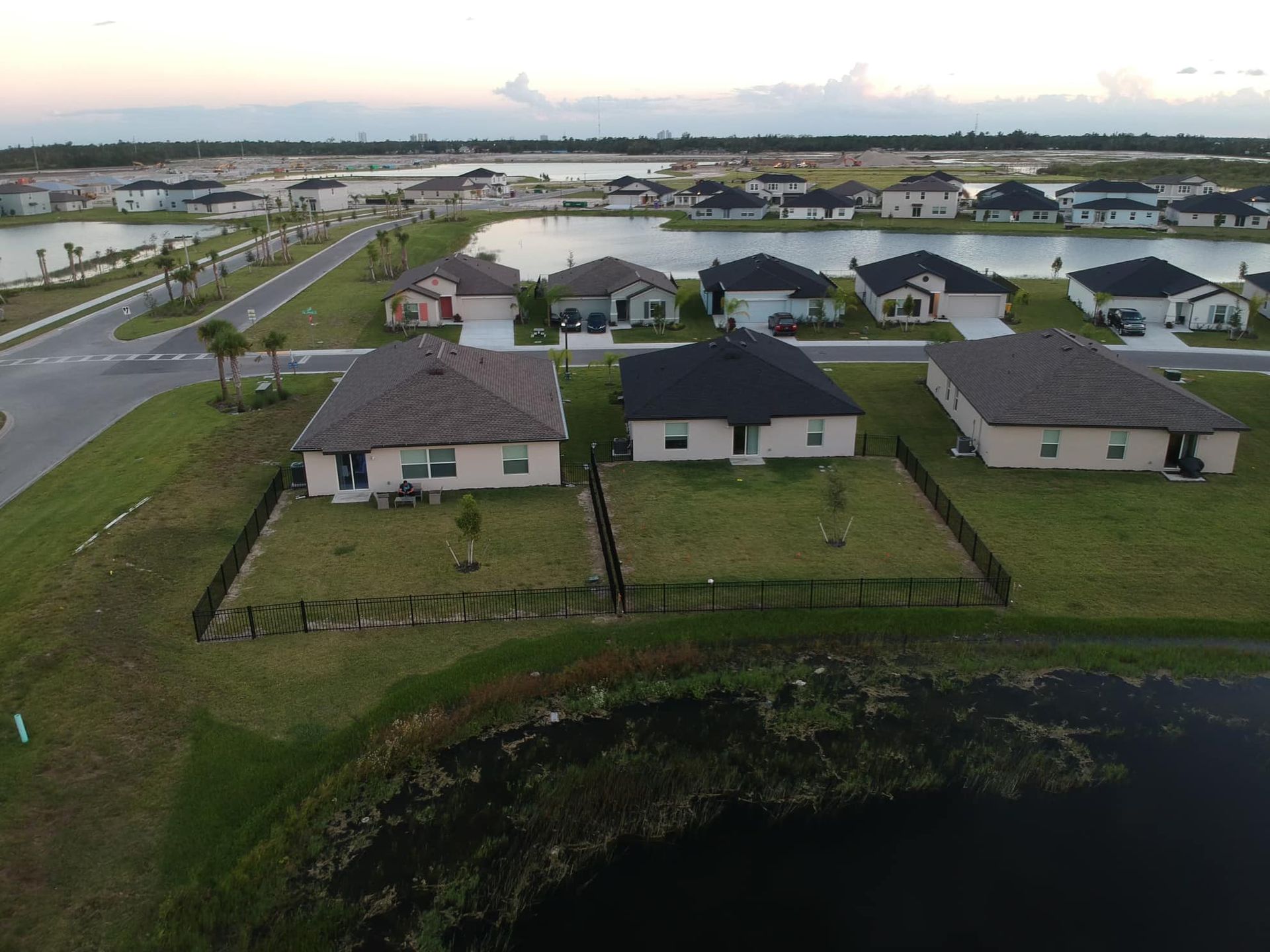 Suburban homes with dark roofs and tan walls sit by a lake under a cloudy sky.