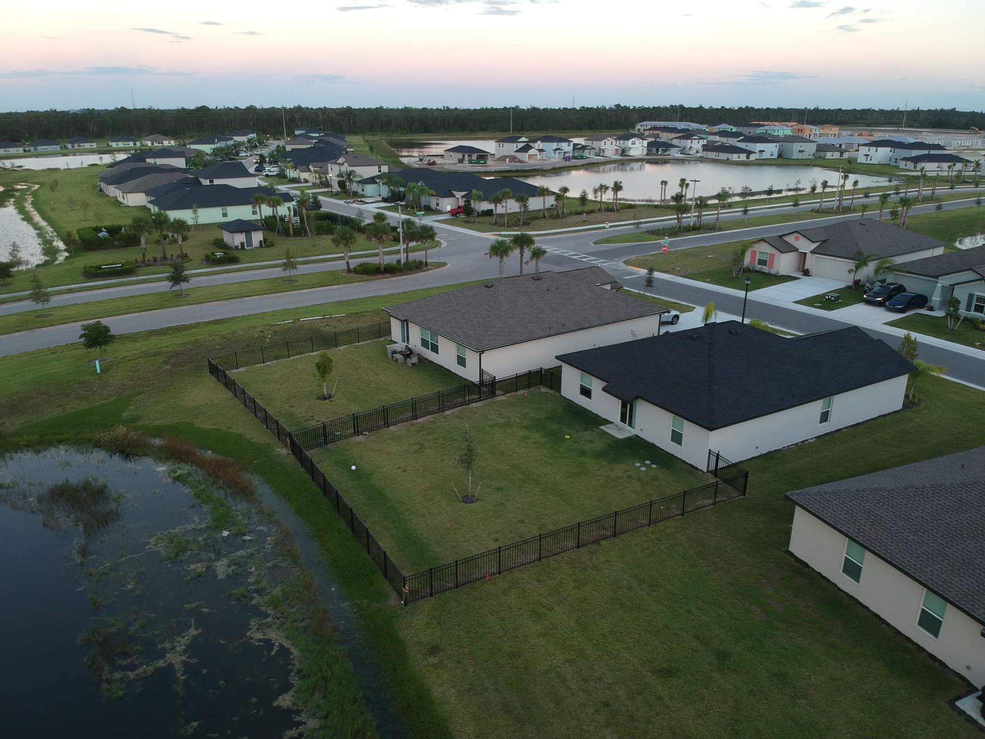 Aerial view of suburban homes near a lake and roads at dusk.