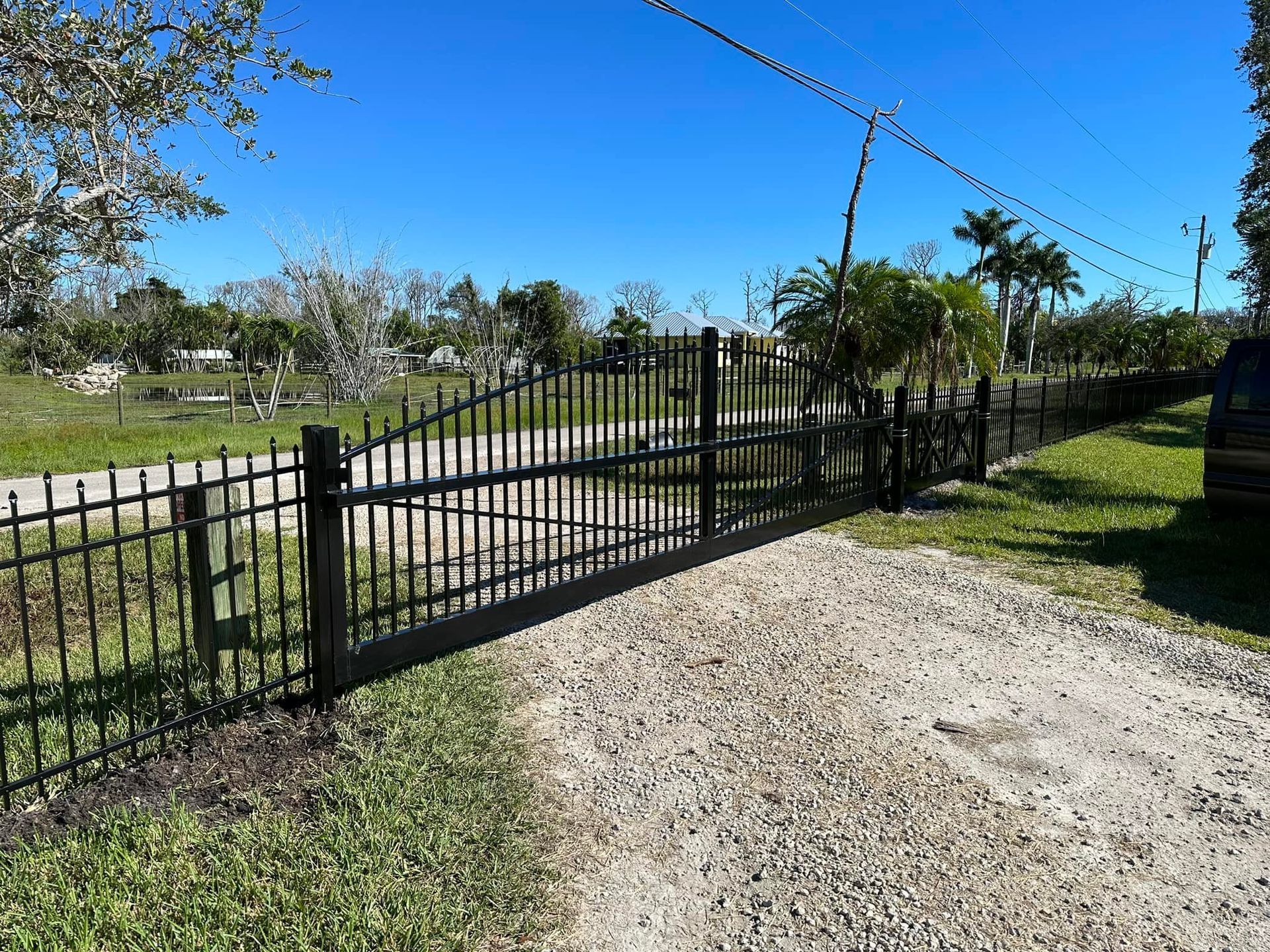Black metal gate and fence on a gravel driveway, with a clear blue sky in the background.