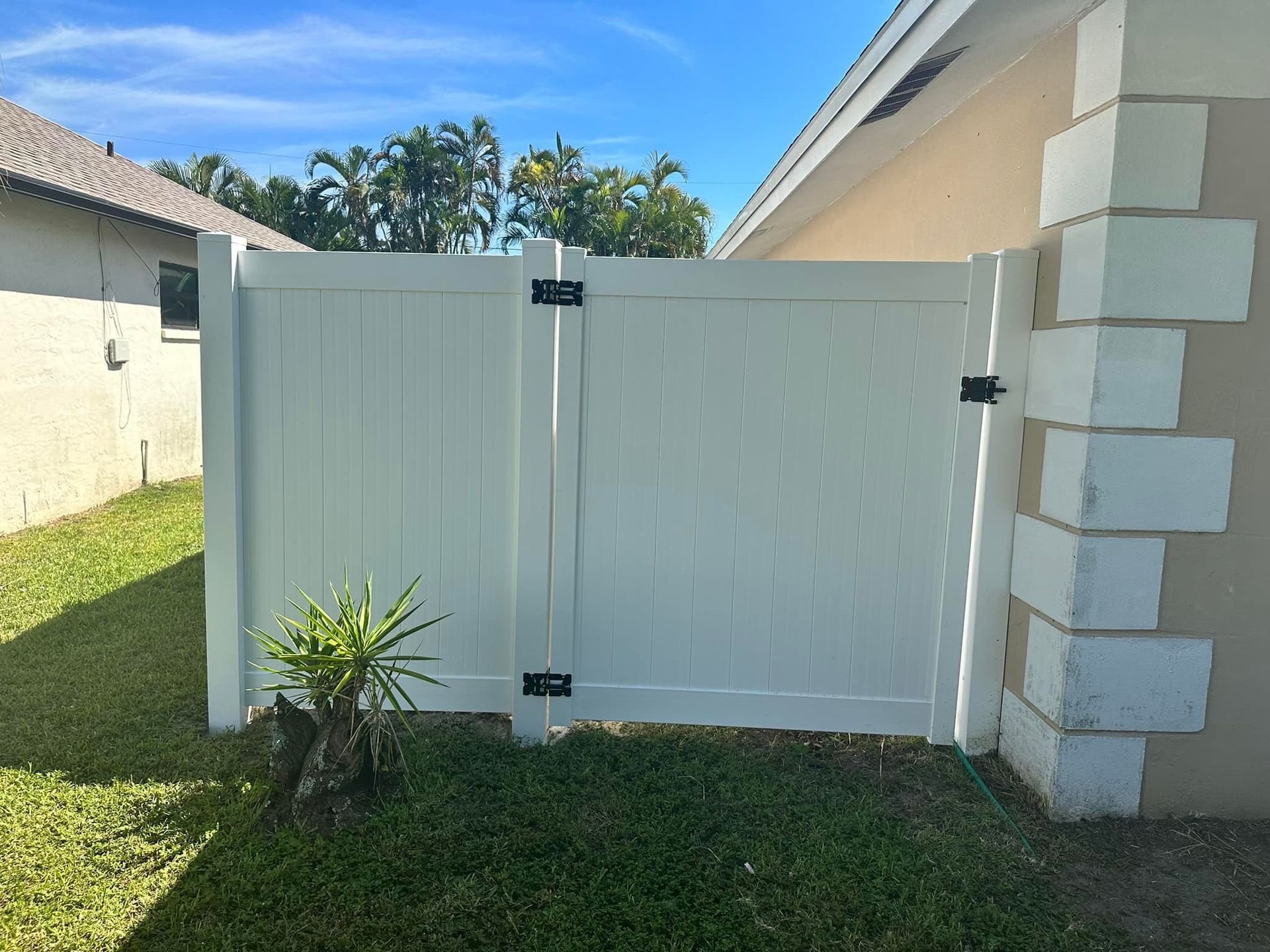 White vinyl fence with a gate next to a concrete block wall, in a grassy yard.