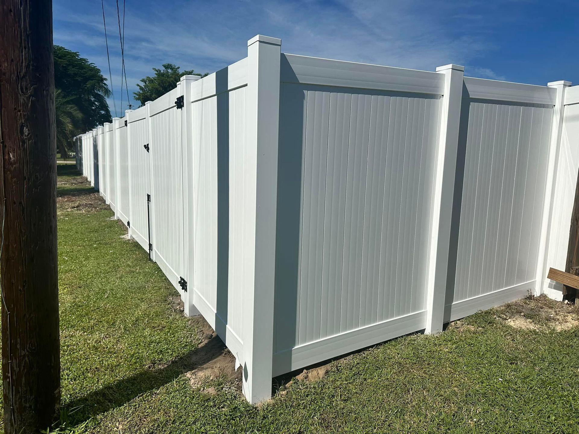 White vinyl privacy fence enclosing a grassy area, under a blue sky.