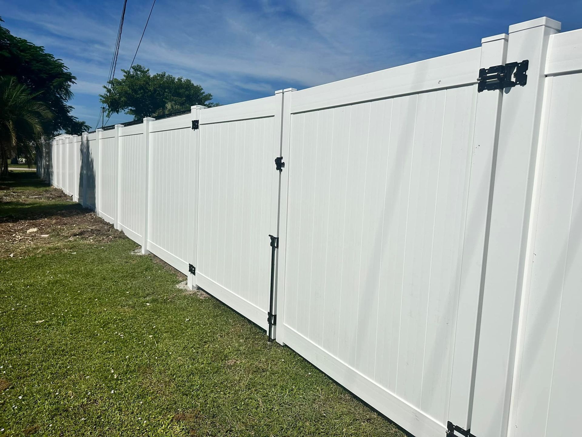 White vinyl fence with gate in a grassy yard under a blue sky.