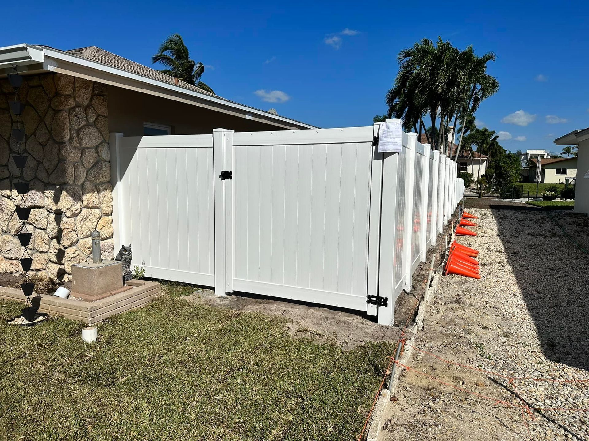 White vinyl fence along a walkway next to a house; orange cones are present.