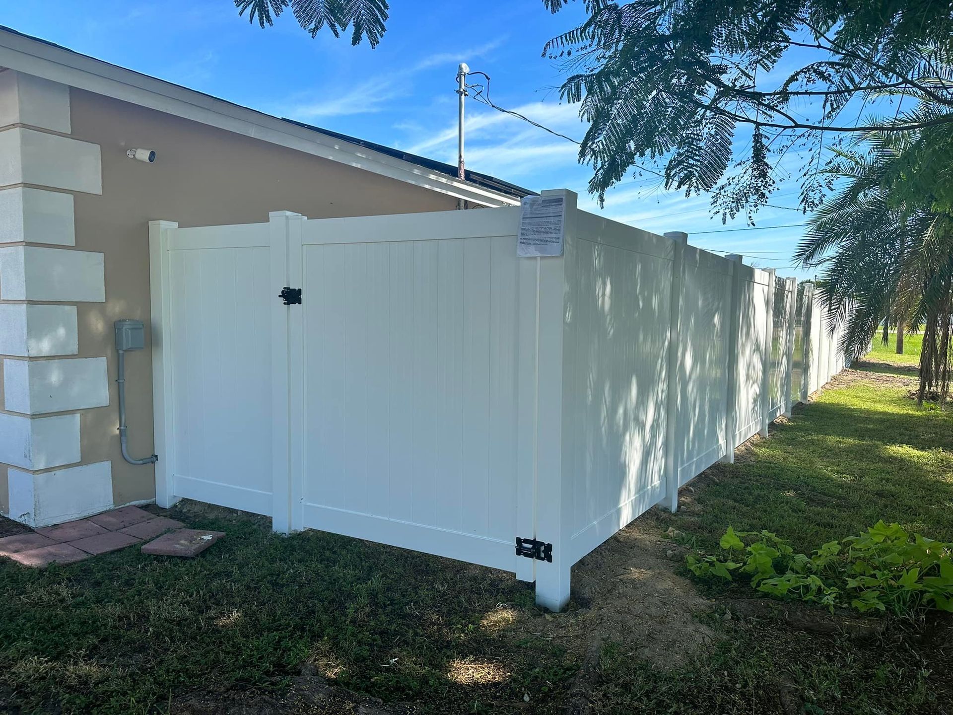 White vinyl fence surrounding a grassy backyard, attached to a beige house on a sunny day.