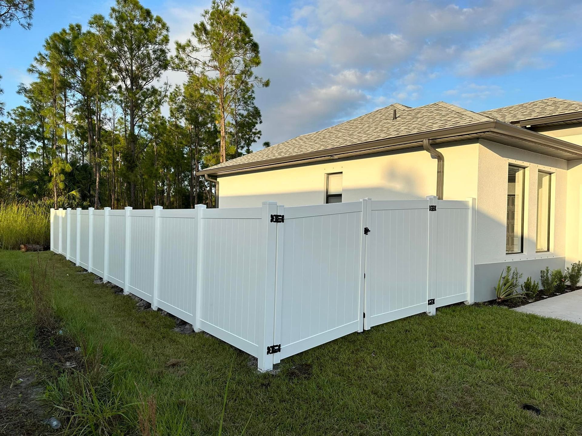 White vinyl fence surrounding a house, on a grassy lawn under a cloudy sky.