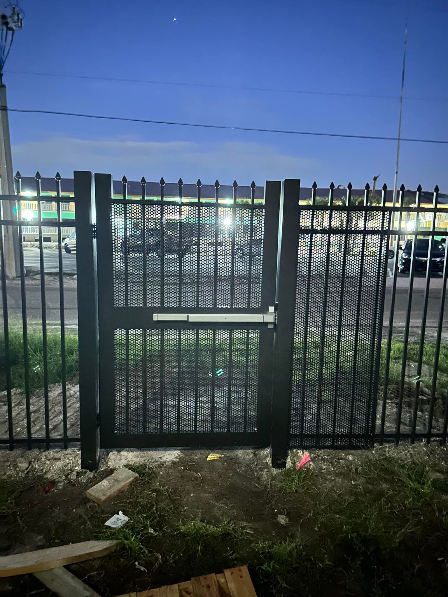 Black metal gate and fence with a decorative center, set against a street at night.