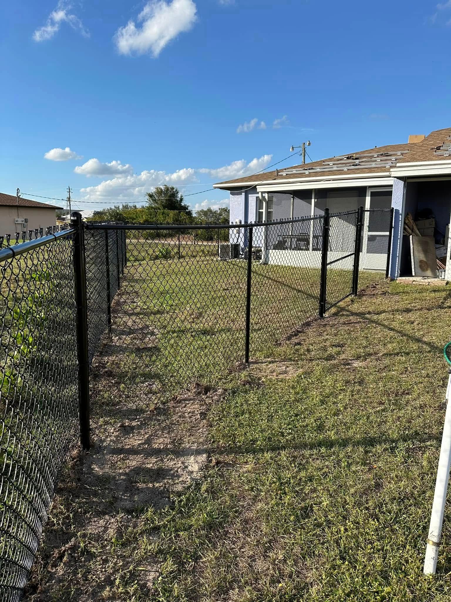 Black chain link fence in a yard, sunny day. Blue house in background.