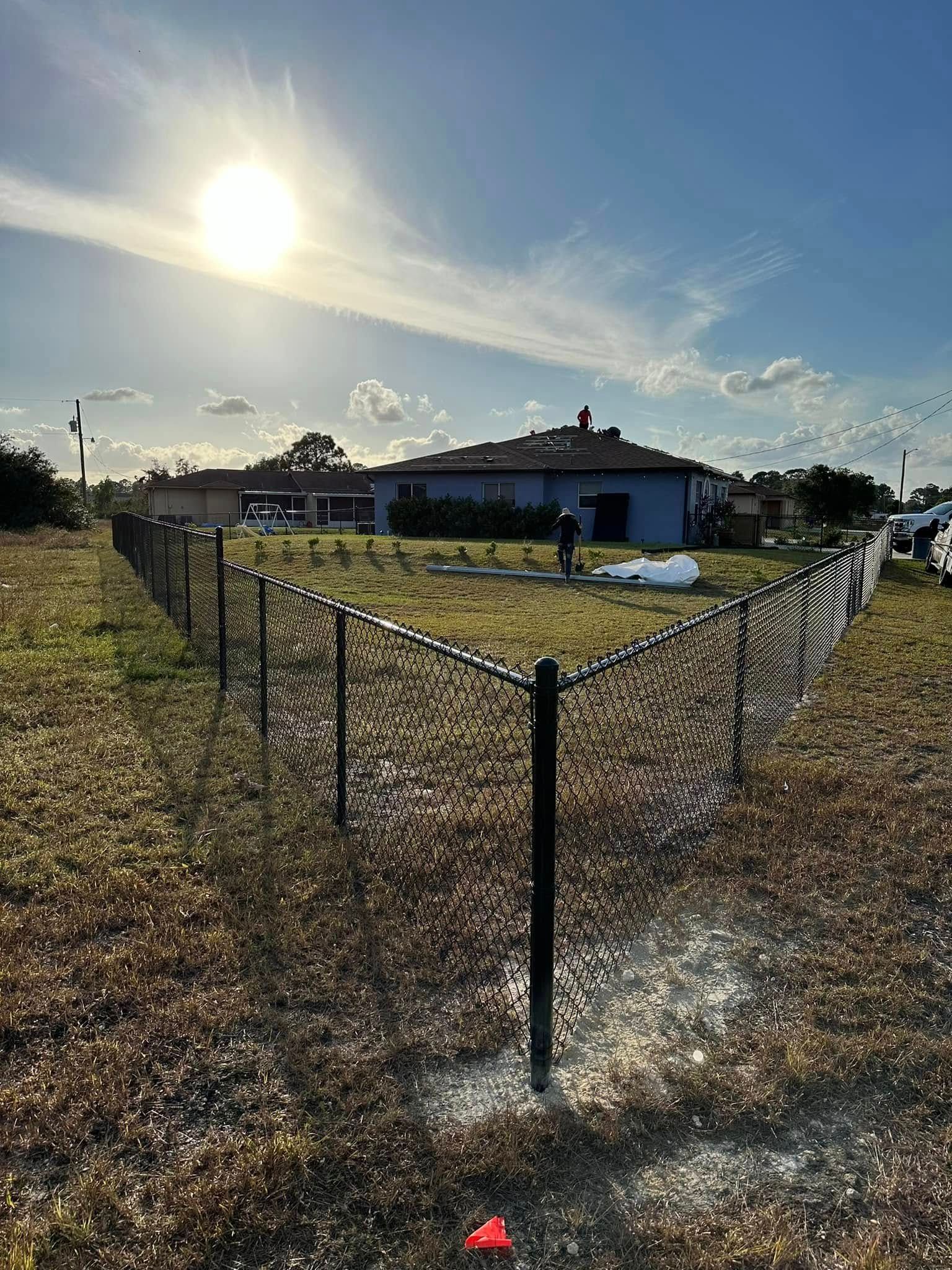 Black fence enclosing a grassy yard with a house in the background under a sunny sky.