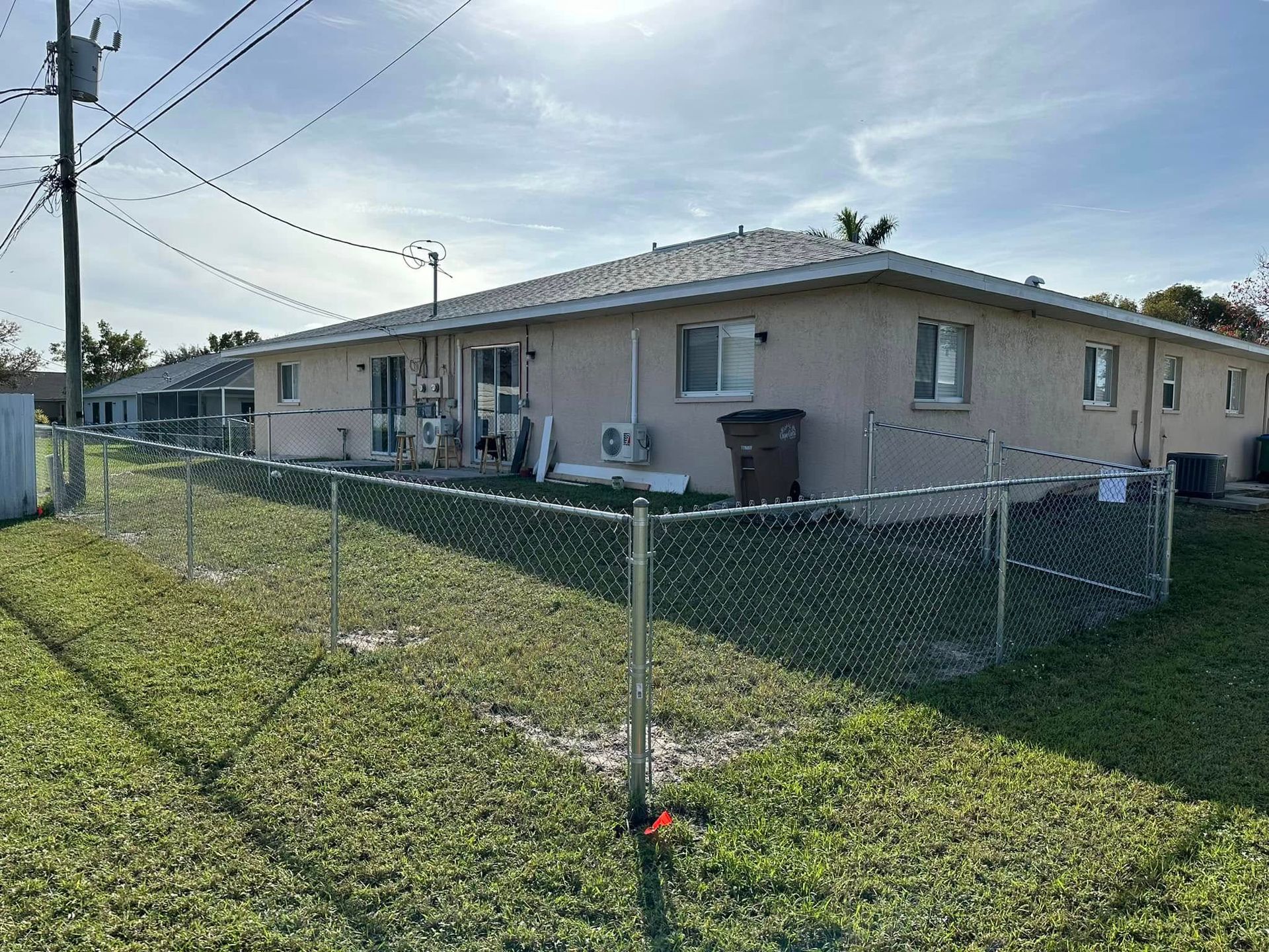 Exterior view of a tan-colored building with a chain-link fence in front and a cloudy sky overhead.