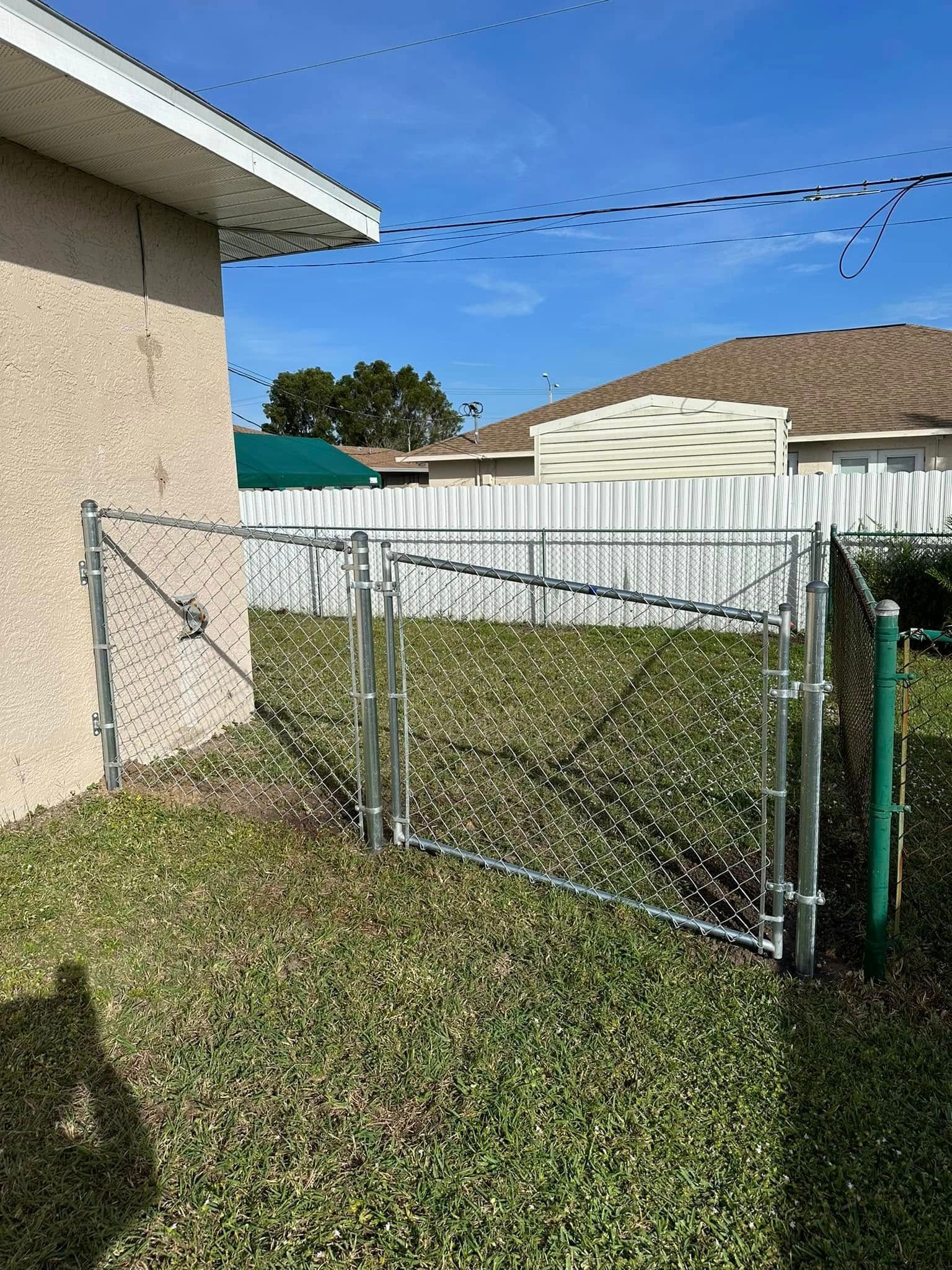 Chain link fence with gate in a grassy yard next to a stucco building.