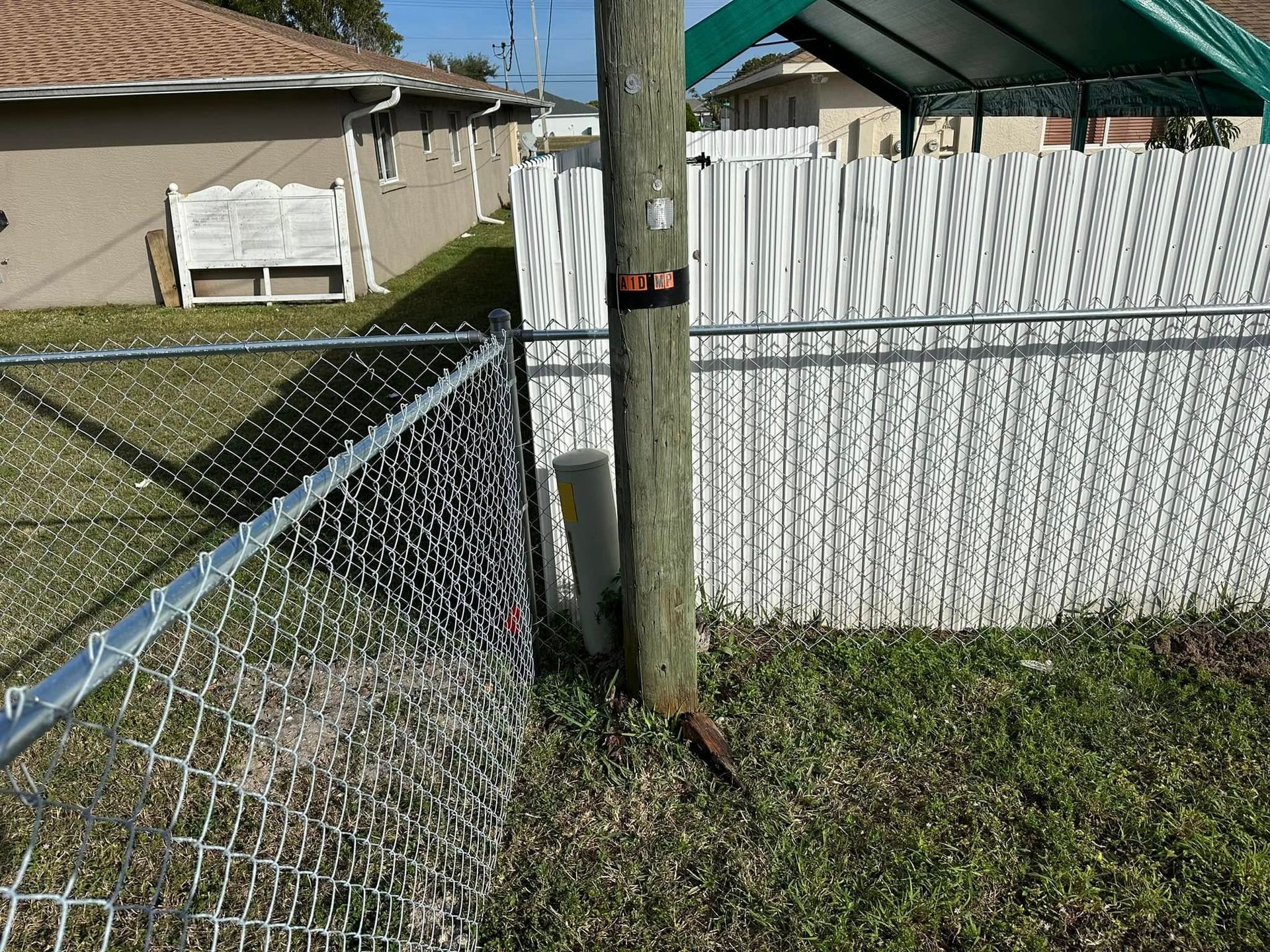 A wooden utility pole sits next to chain-link and white picket fences in a grassy yard.