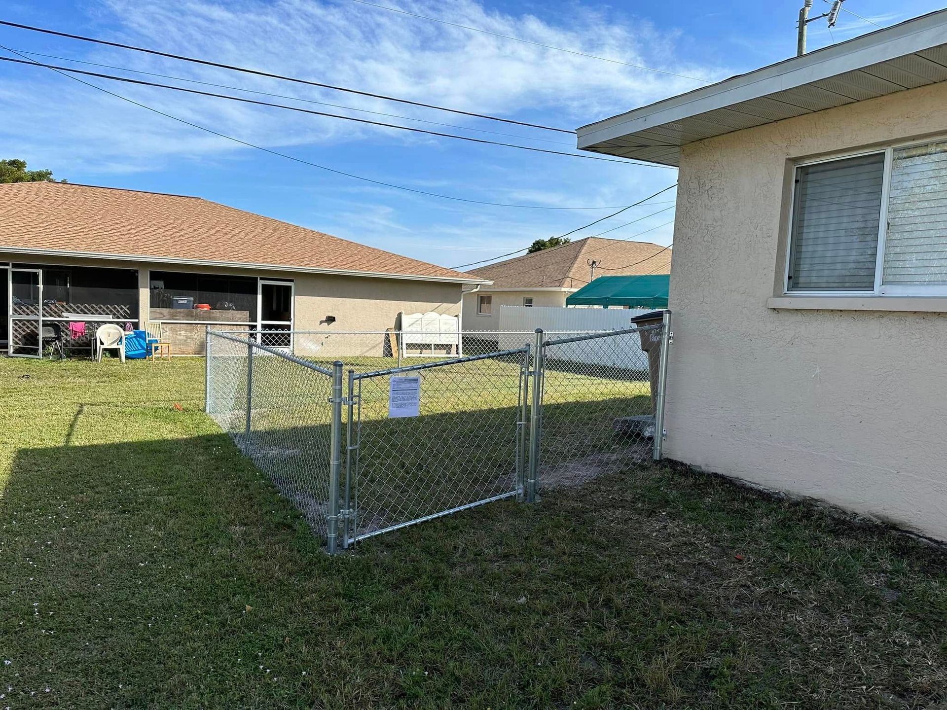 Backyard view with chain-link fence, beige house, and neighboring houses on a sunny day.