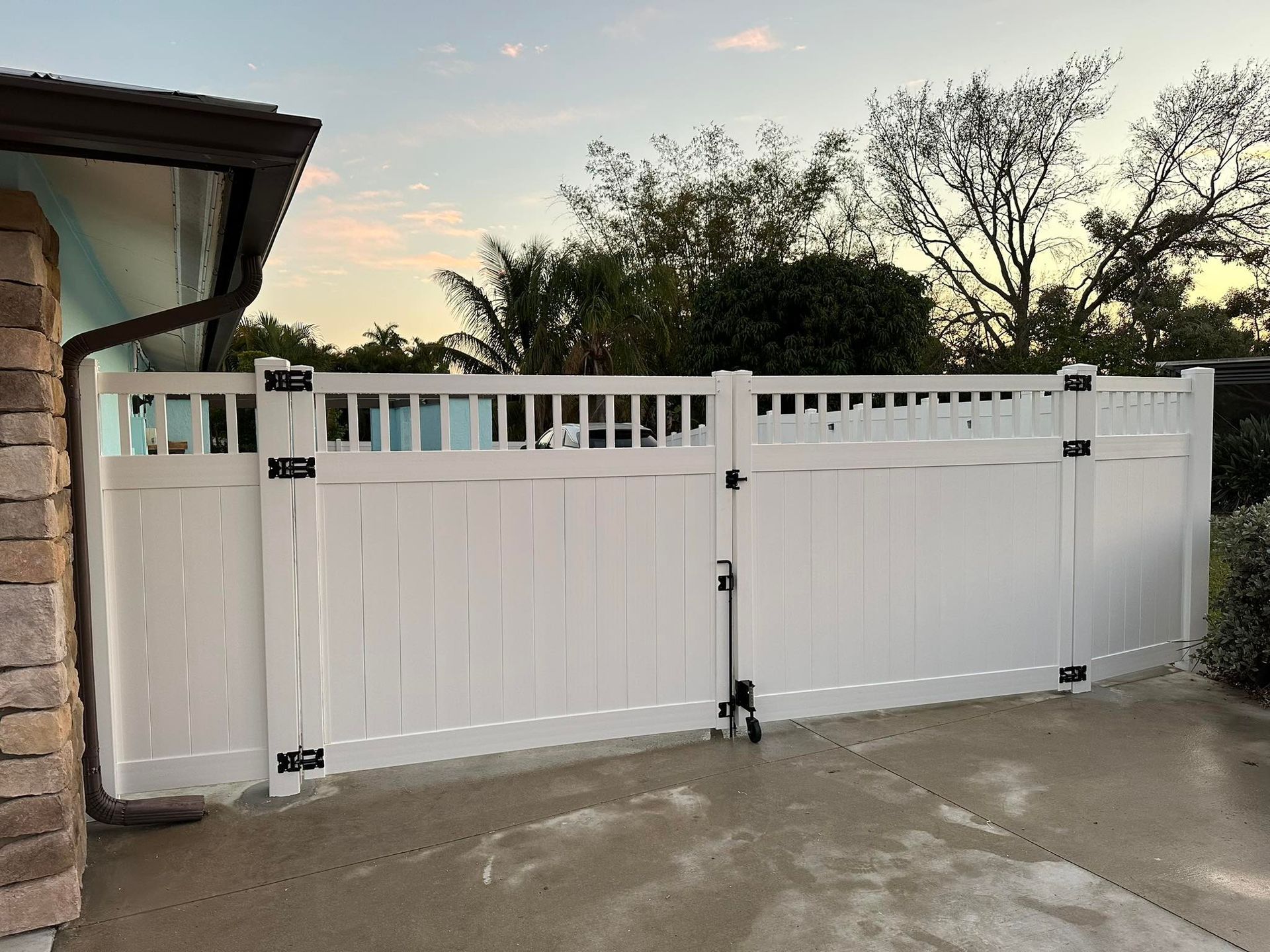 White vinyl fence with gate, black hardware, set against a cloudy sky.