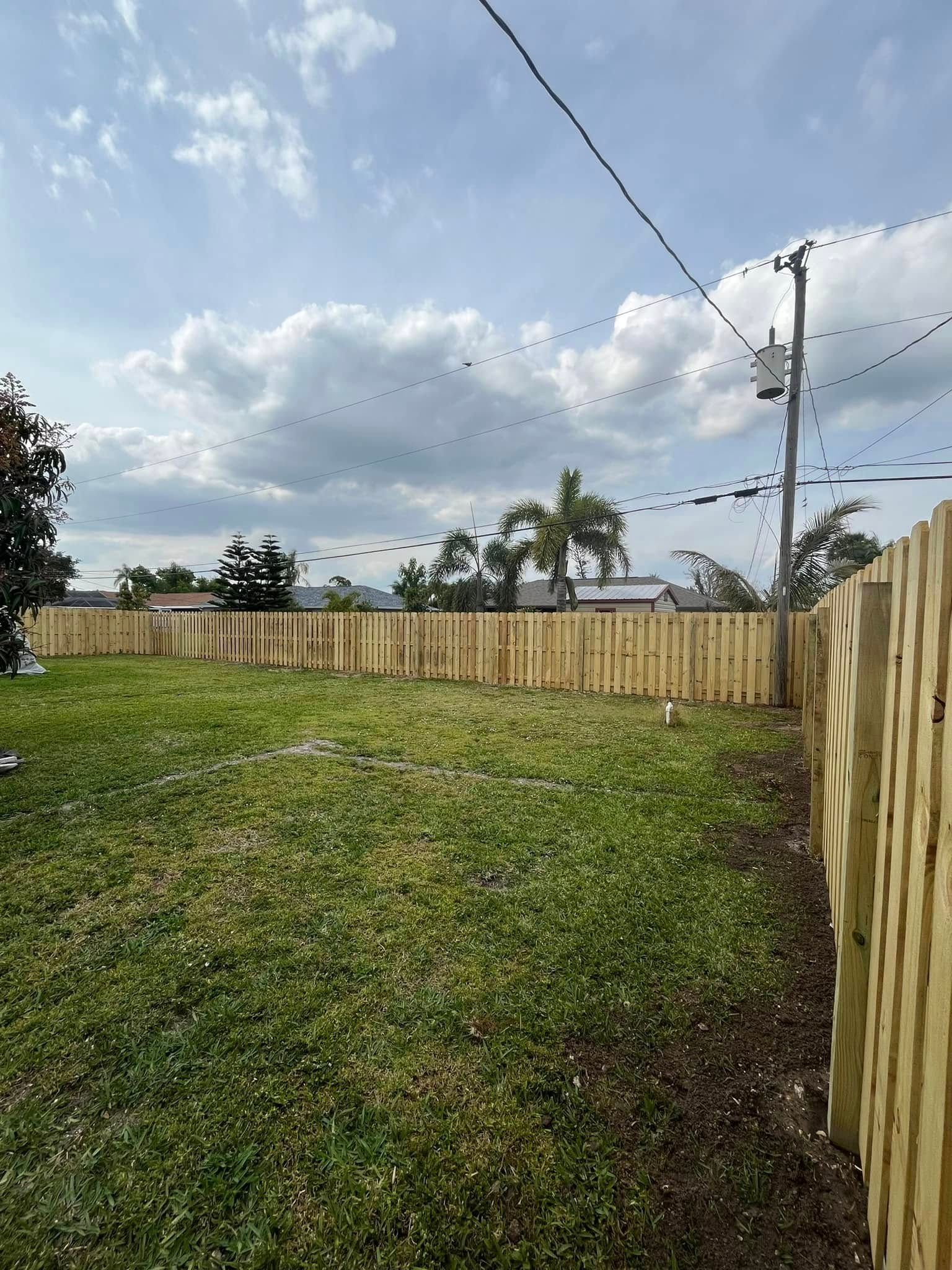 Wooden fence encloses a green backyard under a cloudy sky.