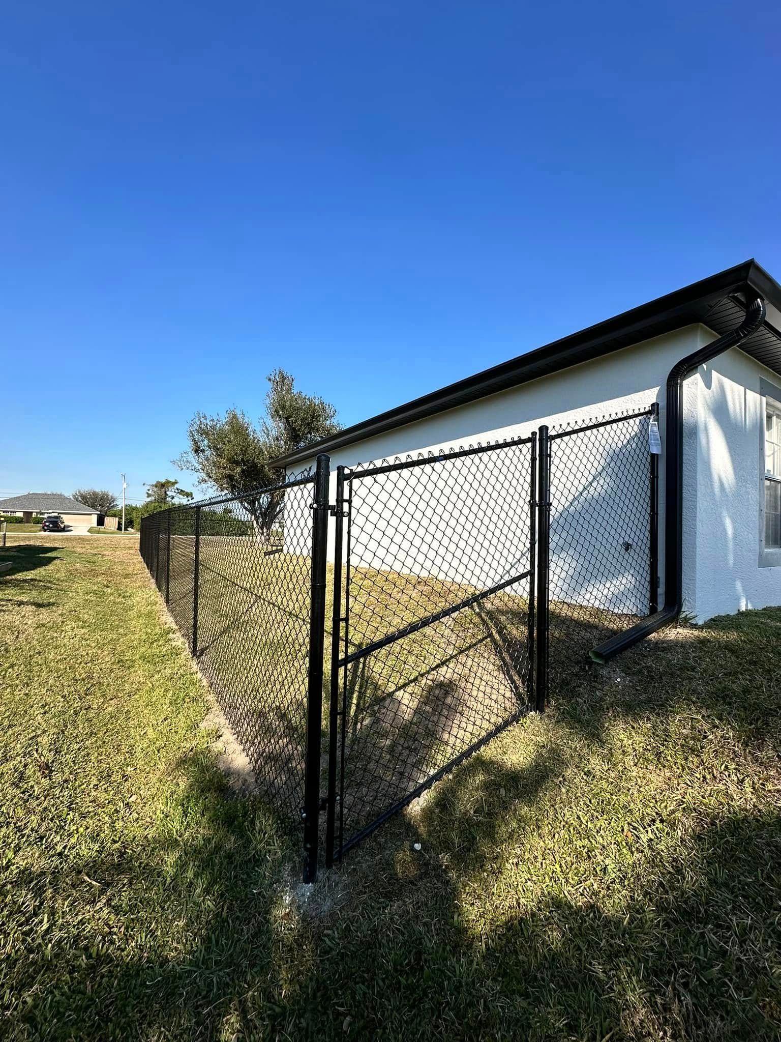 Black metal fence with gate next to a white building, on grassy land under a blue sky.