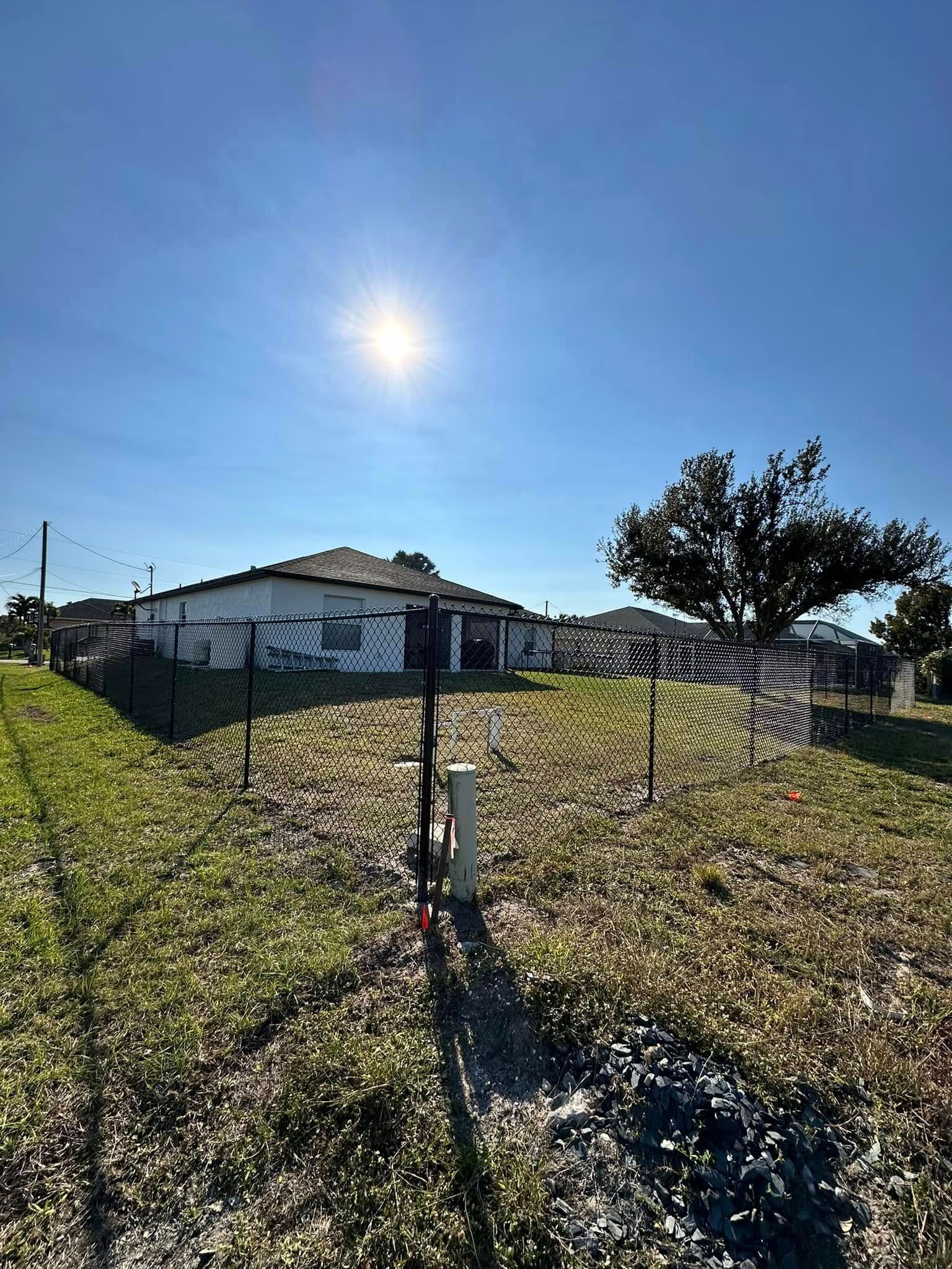 A sunny day view of a house behind a fence, with the sun shining bright overhead.