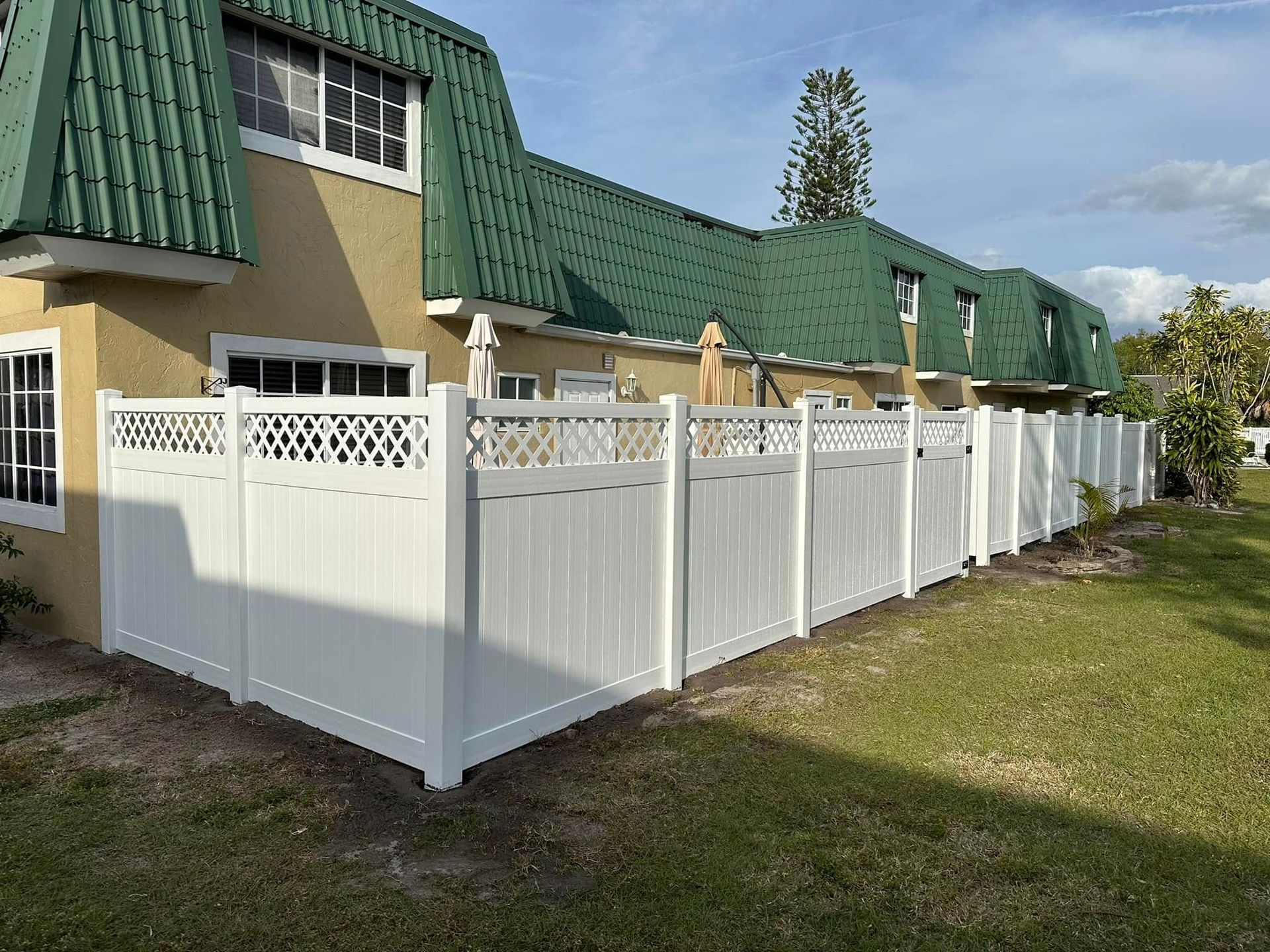 White vinyl fence along a row of townhouses with green roofs. Sunny day.