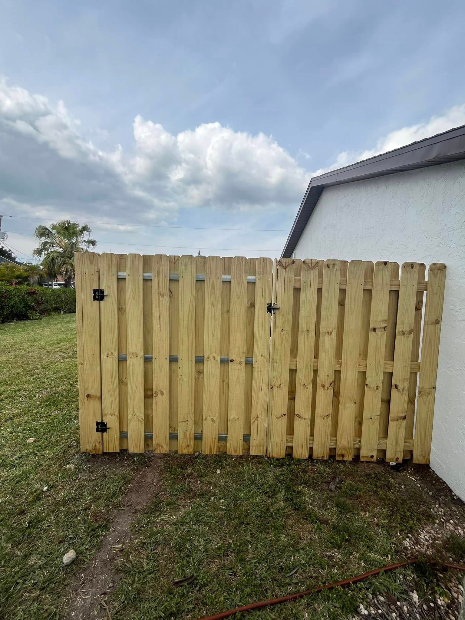 Wooden fence and gate outside a white building, cloudy sky.