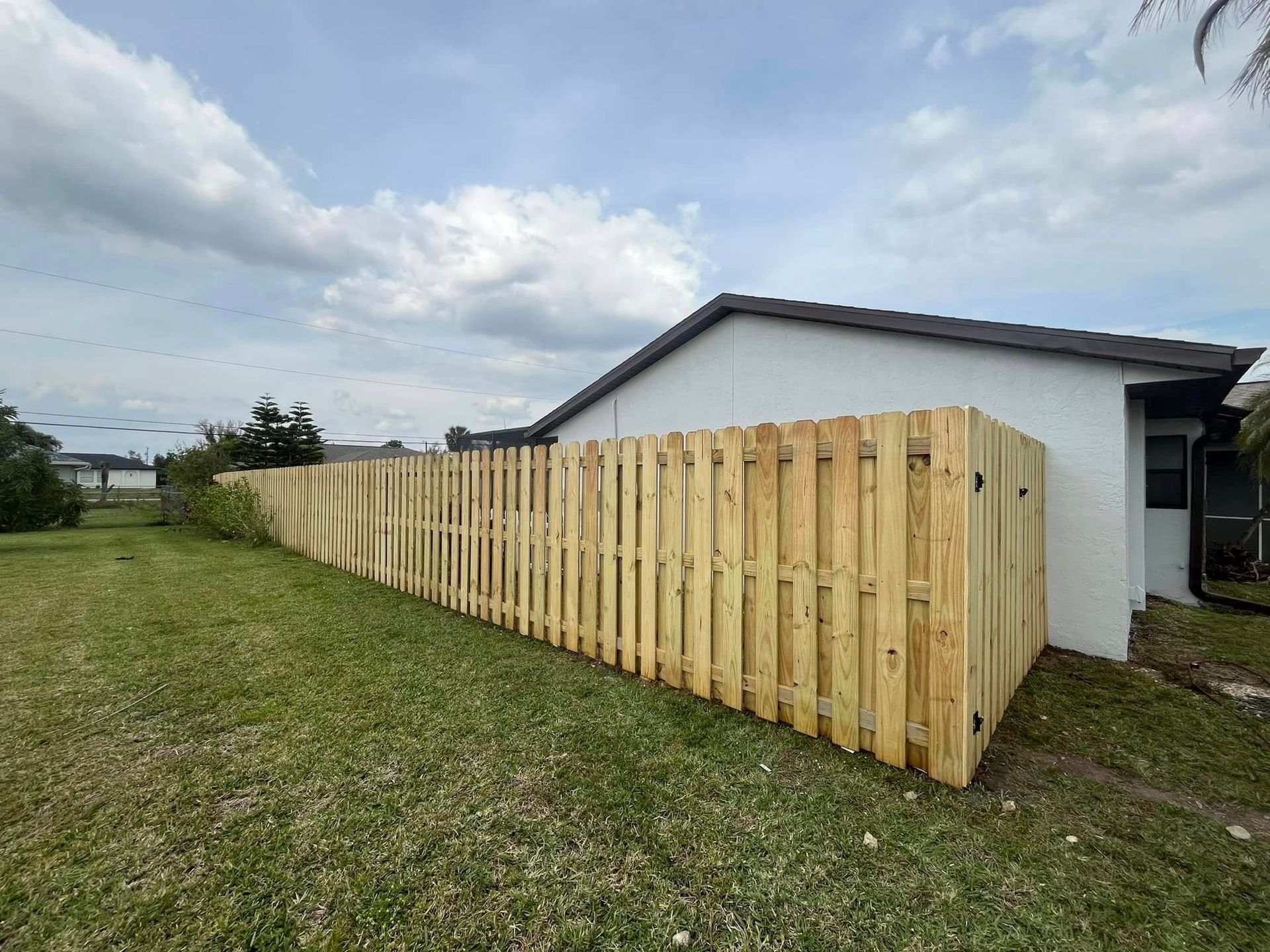Wooden fence in a grassy yard next to a house with a cloudy sky above.